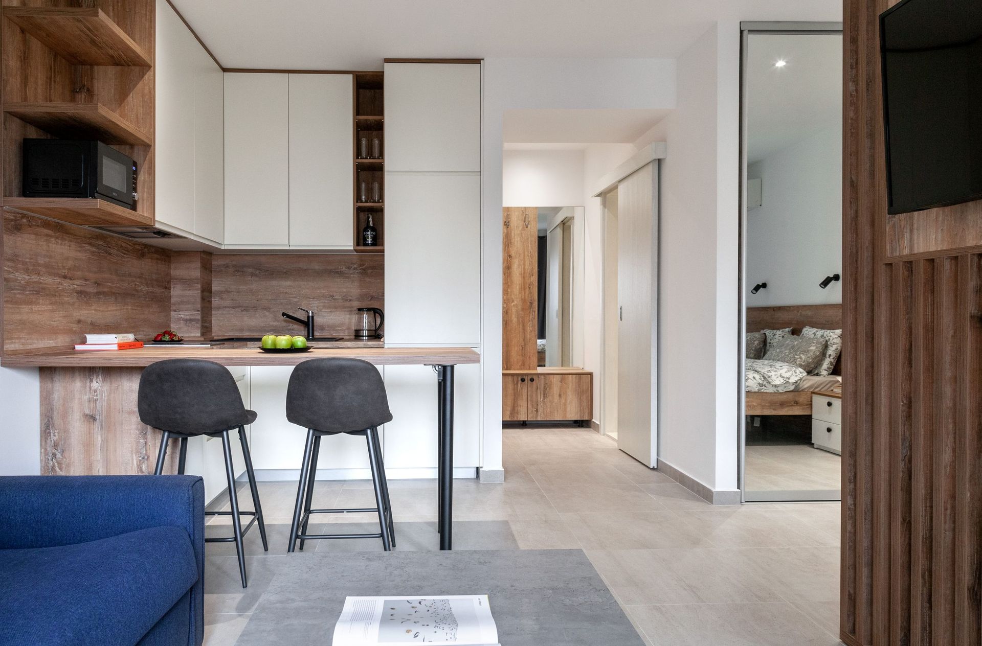 Modern studio kitchen with a bar counter in an apartment in Kotor, Montenegro: light furniture, wood, and a view of the bedroom.