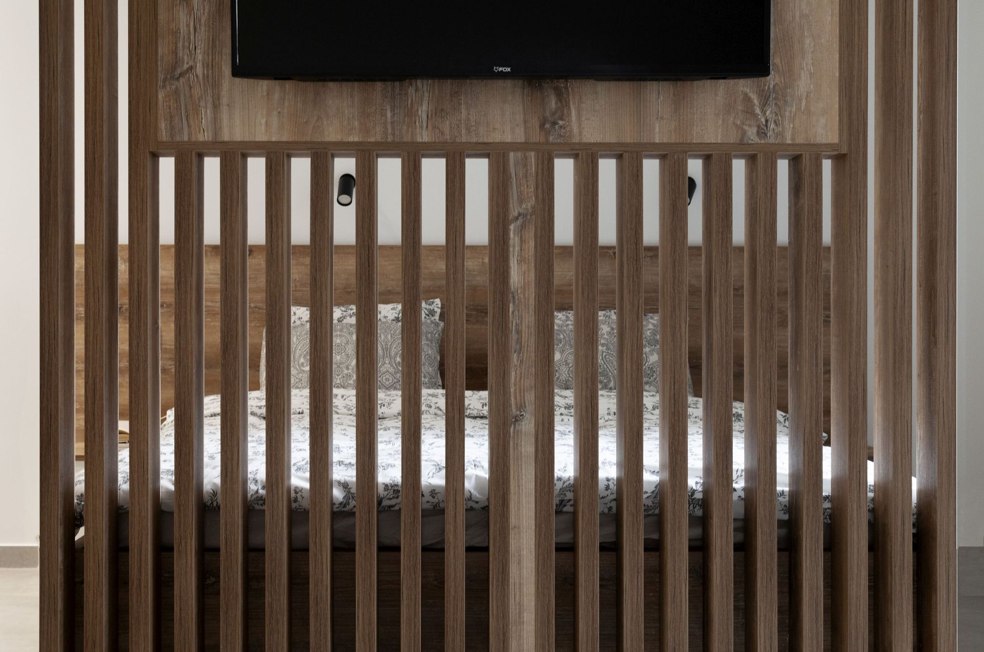 Modern bedroom in an apartment in Kotor, Montenegro: bed behind a decorative wooden partition with a TV panel.