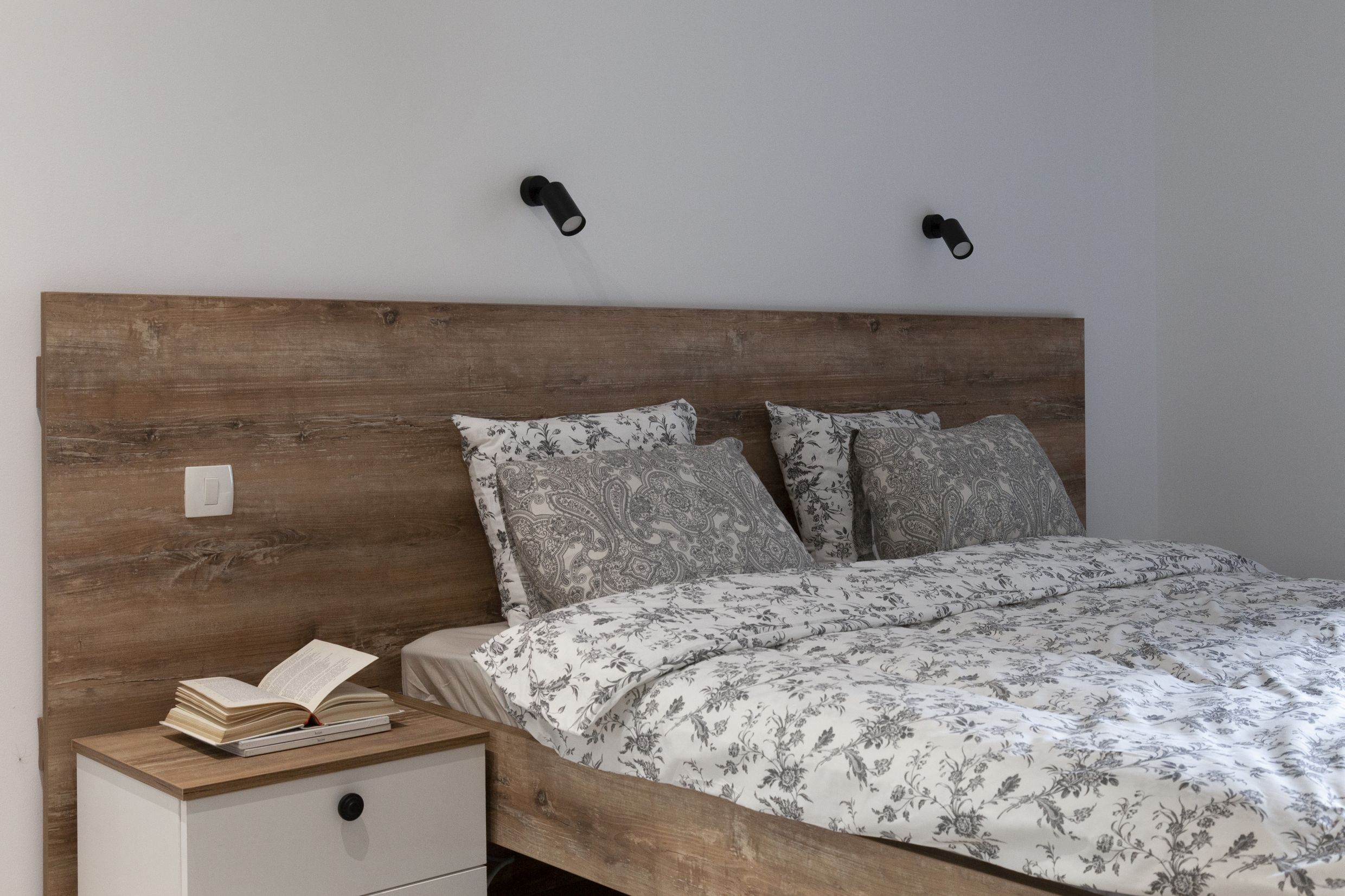 Modern bedroom with a wooden headboard in an apartment in Kotor, Montenegro. Cozy interior with white furniture.