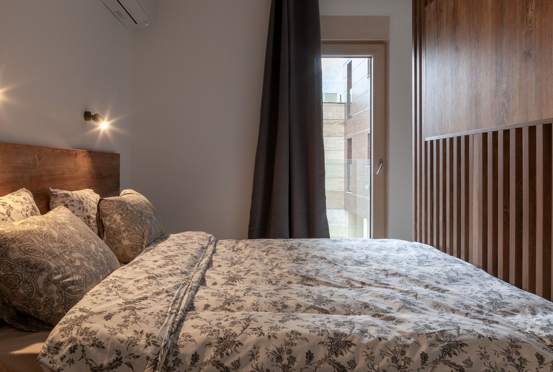 Modern bedroom in an apartment in Kotor, Montenegro: double bed, wood wall paneling, and access to the balcony.