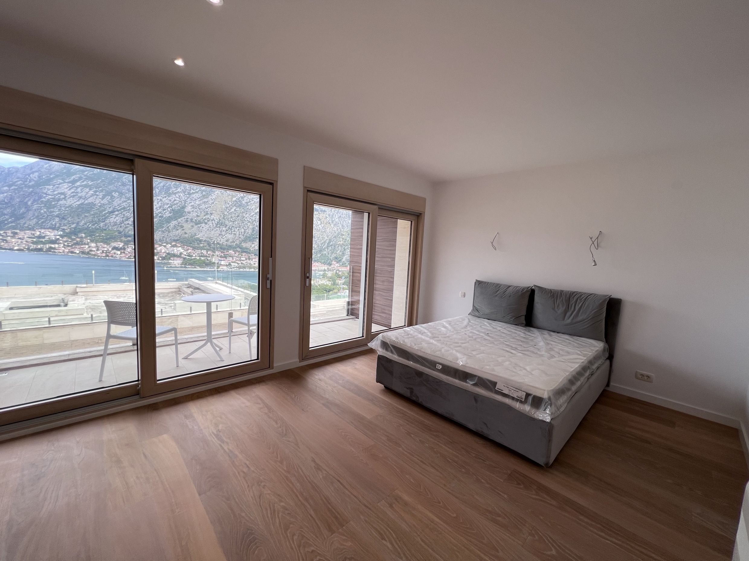 Bedroom in an apartment in Kotor, Montenegro: a double bed, panoramic windows, and a terrace overlooking the Bay of Kotor.