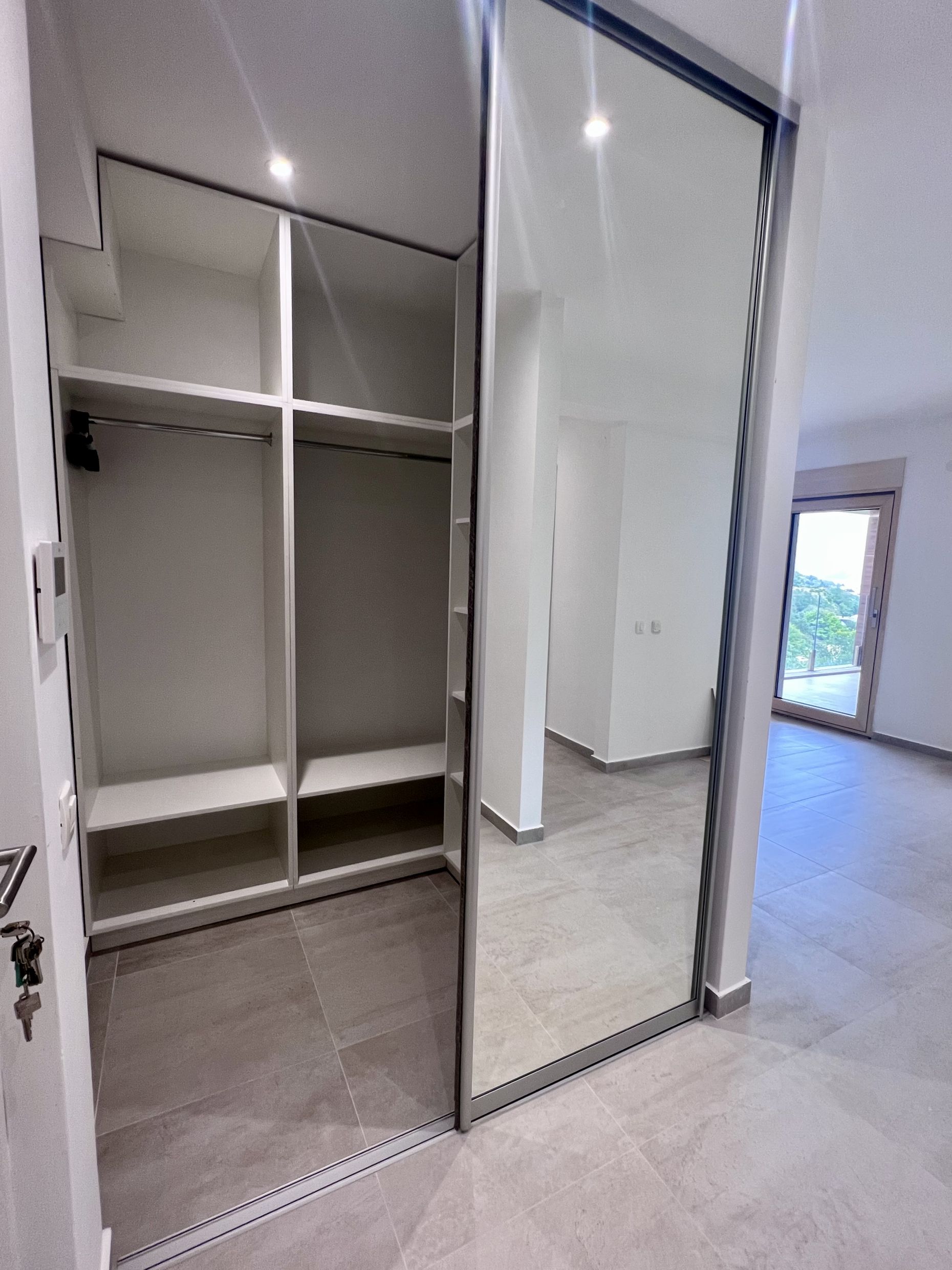 Built-in wardrobe with mirrored doors in a modern bedroom of an apartment in Kotor, Montenegro, with mountain views.