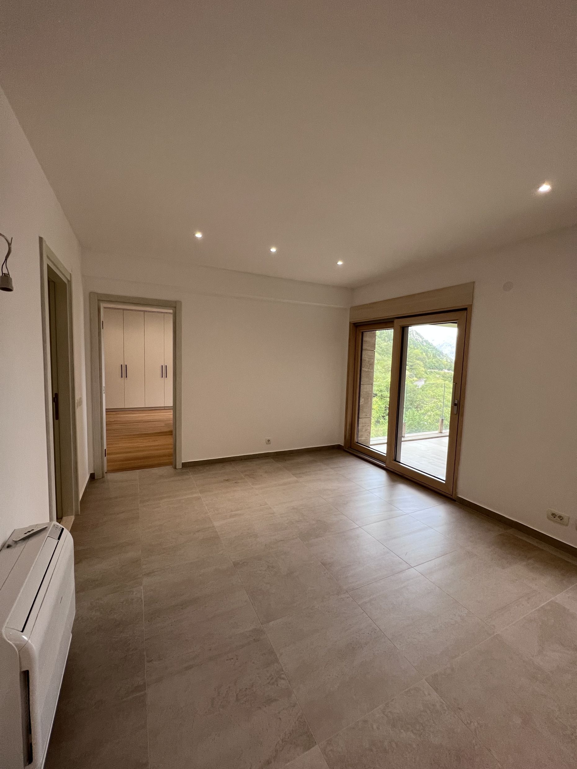 Bright living room with a panoramic window and mountain view in an apartment, Kotor, Montenegro. Modern finishes and tile.