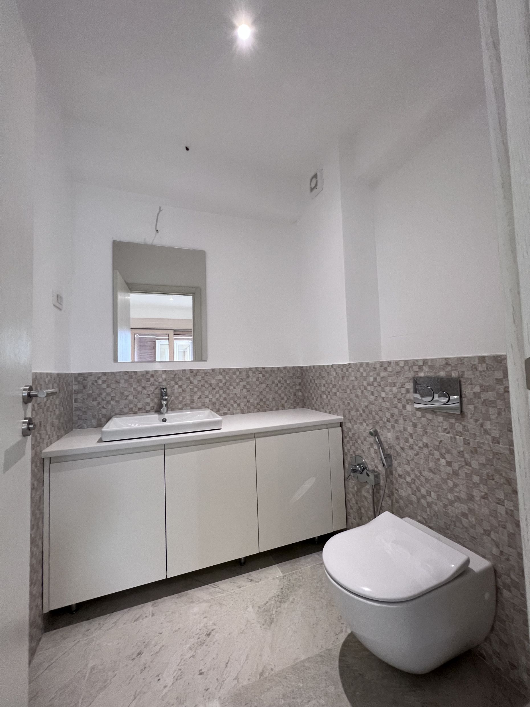 Modern bathroom in an apartment, Kotor, Montenegro: wall-mounted toilet, vanity with sink, and mirror.