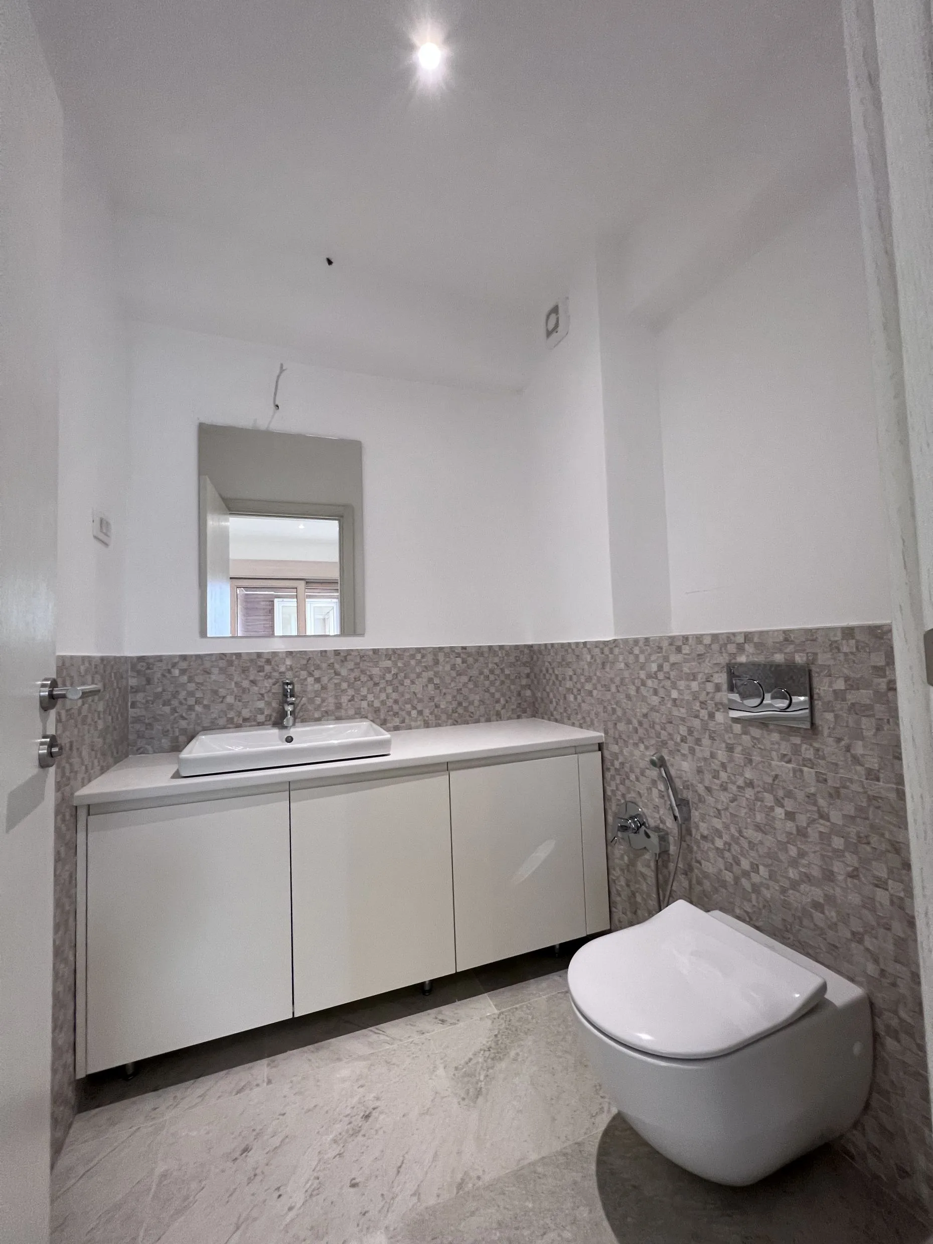 Modern bathroom featuring a wall-mounted toilet, white vanity with a vessel sink, and grey mosaic tile wainscoting.