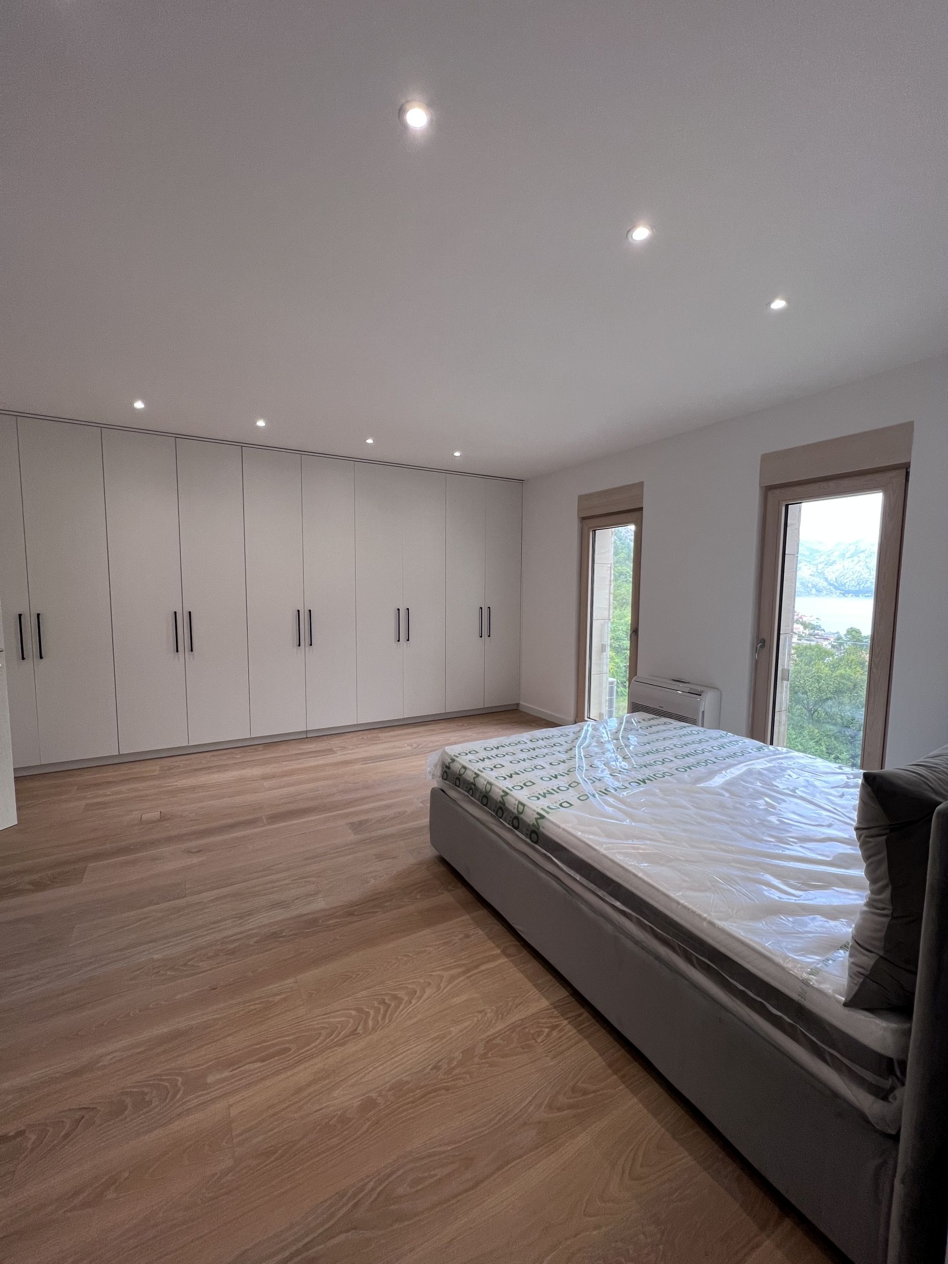 Modern bedroom in Kotor, Montenegro: bed, built-in wall-to-wall wardrobe, parquet flooring, and sea view from the window.