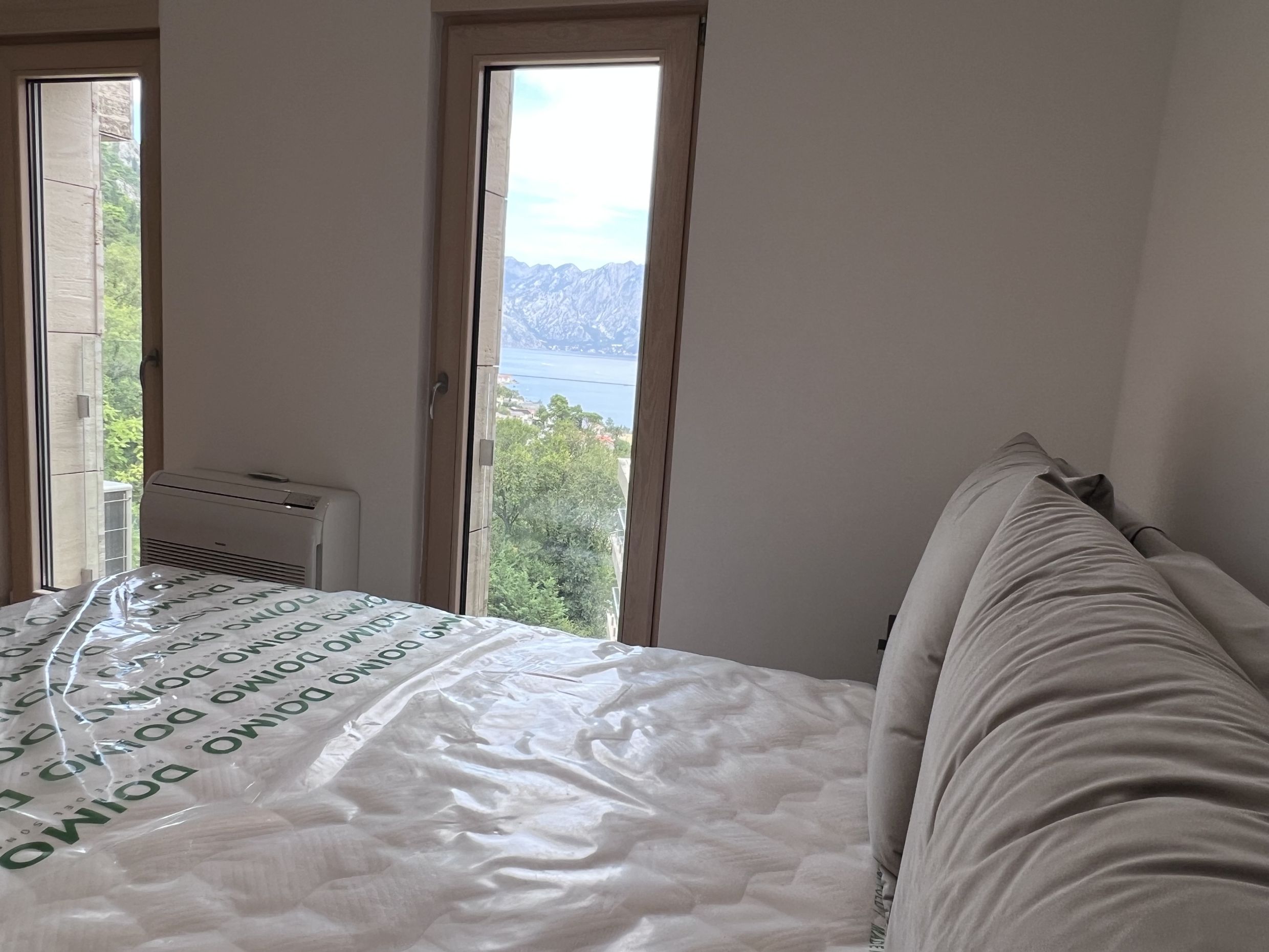 Bedroom in an apartment in Kotor, Montenegro, with panoramic views of Kotor Bay and the mountains through tall windows.