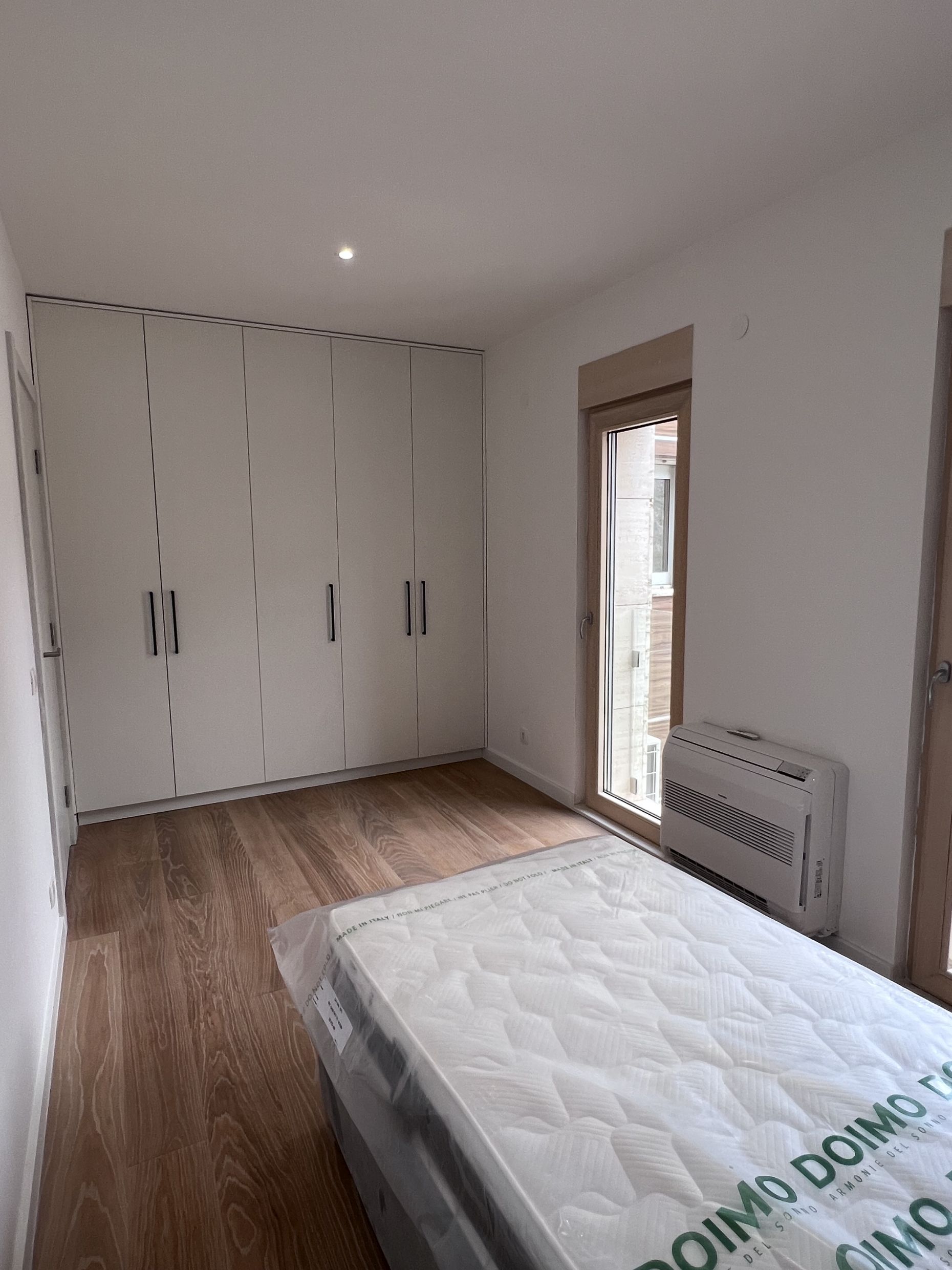 Bedroom in an apartment in Kotor, Montenegro: built-in wardrobe, parquet floor, bed with mattress, and air conditioner.