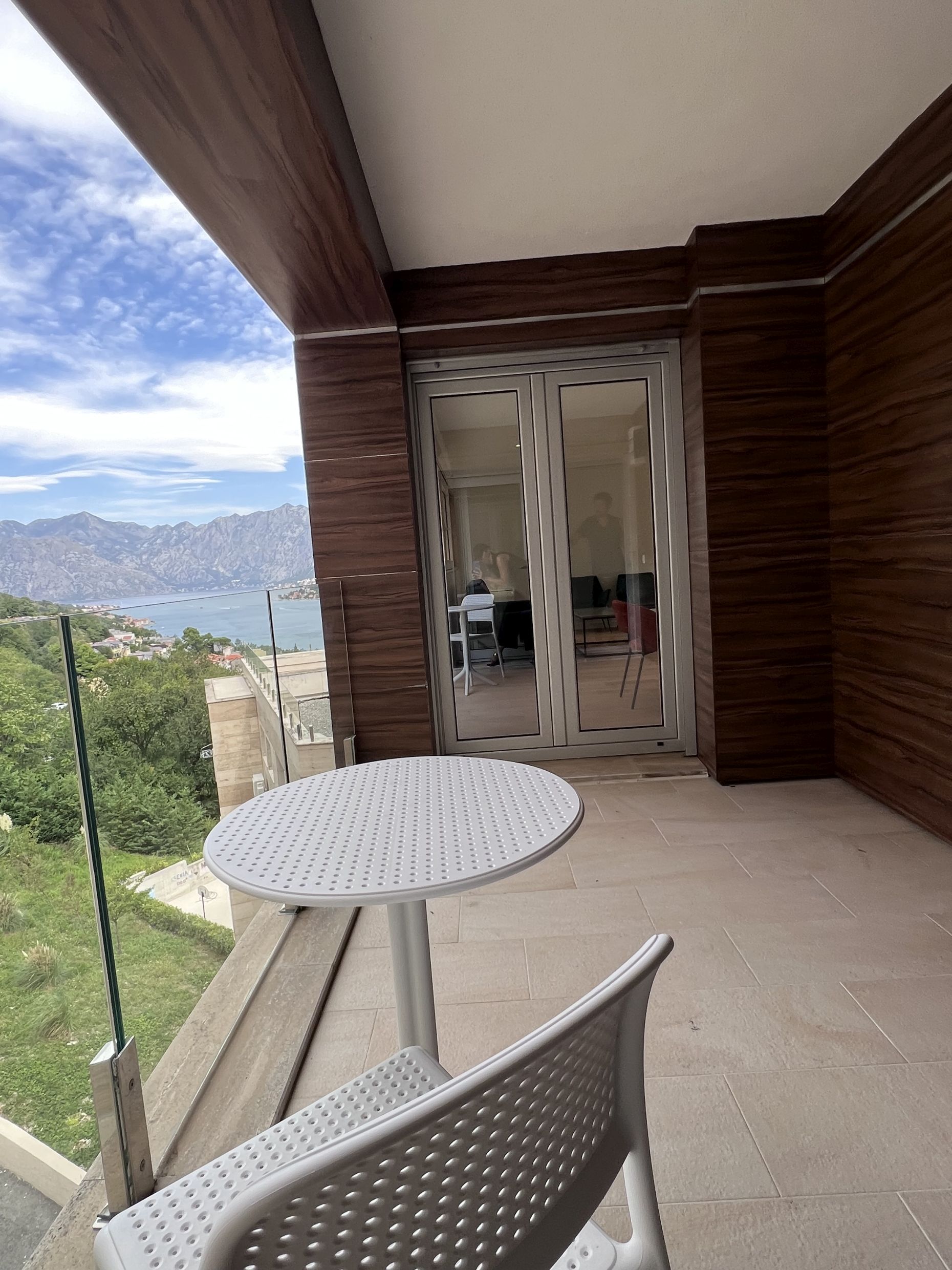 Apartment balcony in Kotor, Montenegro: panoramic view of the Bay of Kotor, modern finishes, and outdoor furniture.