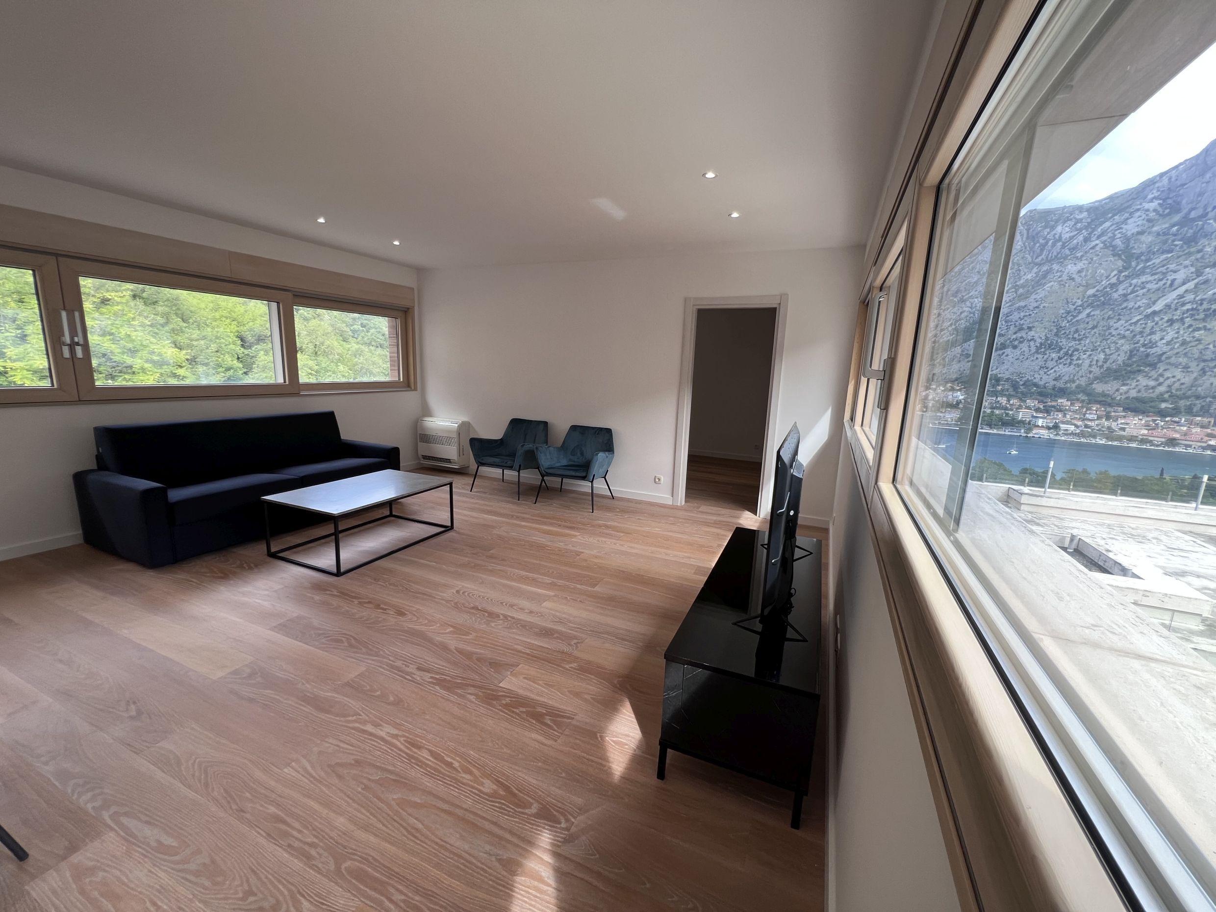 Living room in an apartment in Kotor, Montenegro: modern furniture, panoramic windows with views of the Bay of Kotor and the mountains.