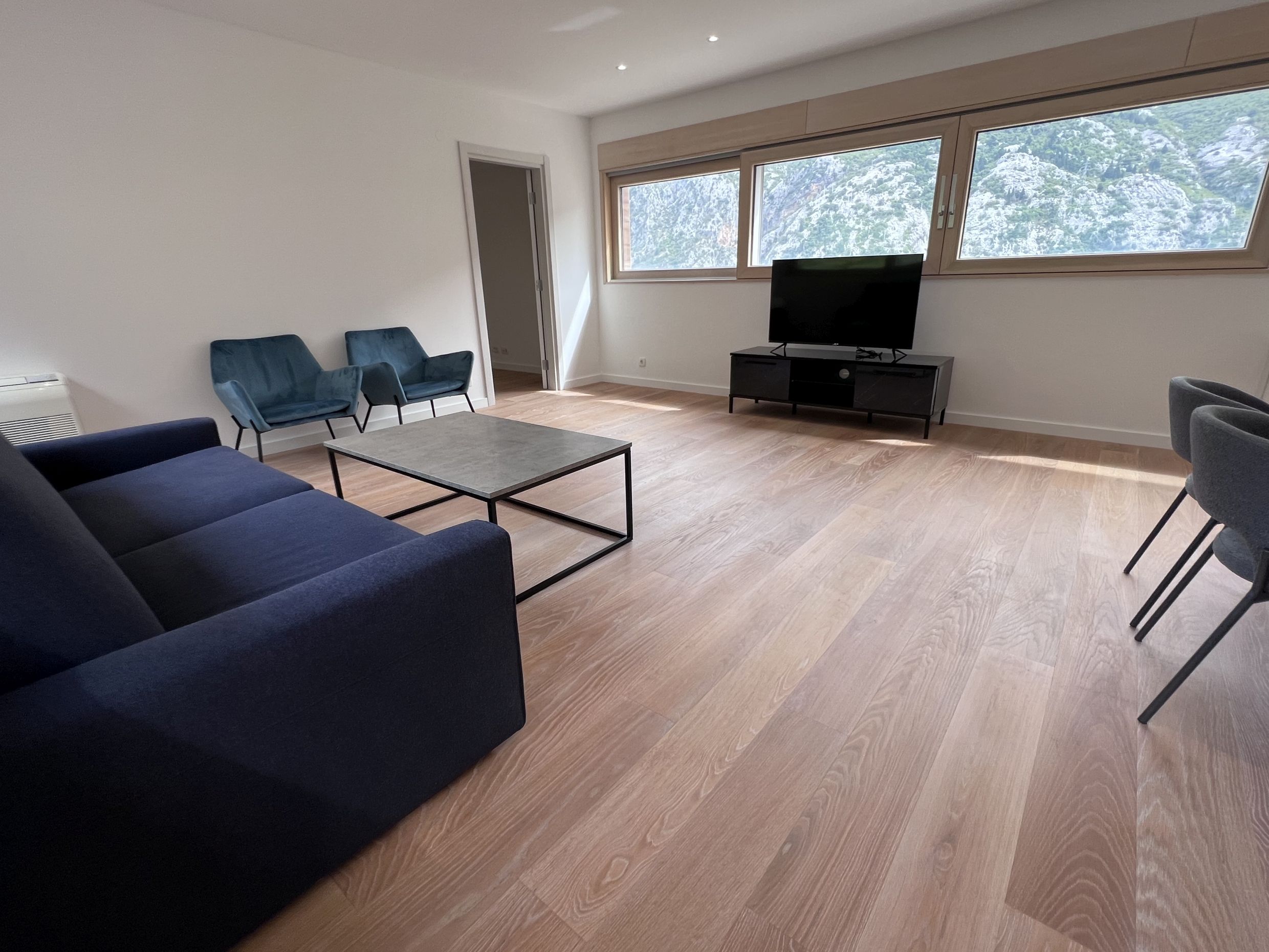 Modern living room in an apartment in Kotor, Montenegro: blue sofa, panoramic windows with mountain views, bright interior.