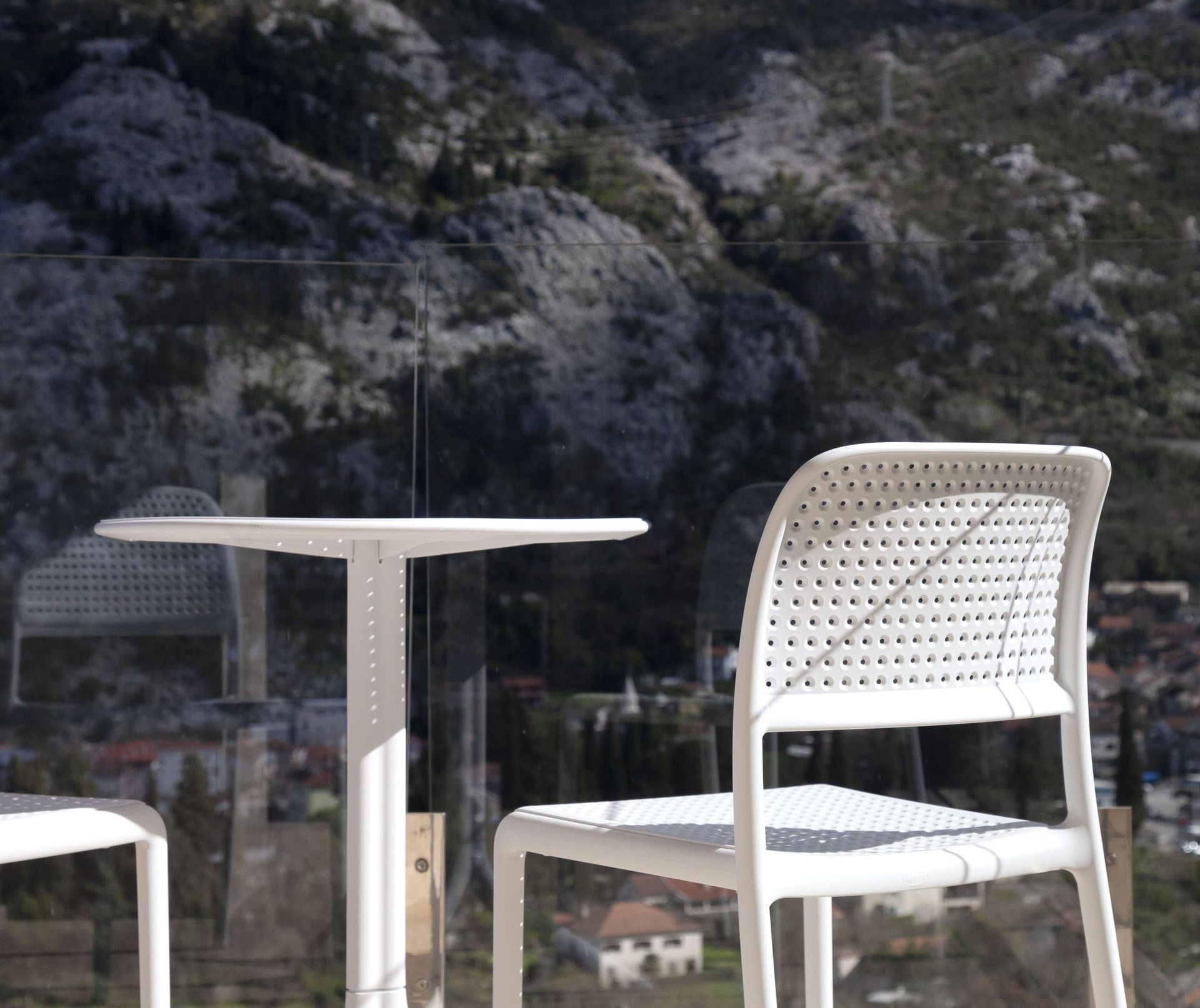 White chairs and a small table on the apartment balcony in Kotor, Montenegro, with panoramic views of the mountains and the city.