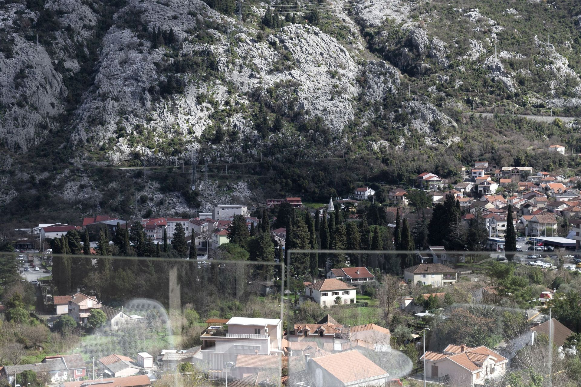 Panoramic view from the apartment window of the mountains and the city of Kotor in Montenegro from a terrace with glass railing.