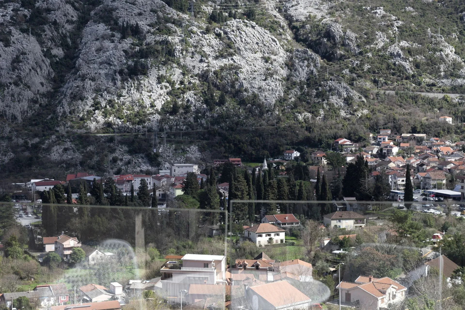 Panoramic view of a town with red roofs at the foot of a rocky mountain, shot through glass.