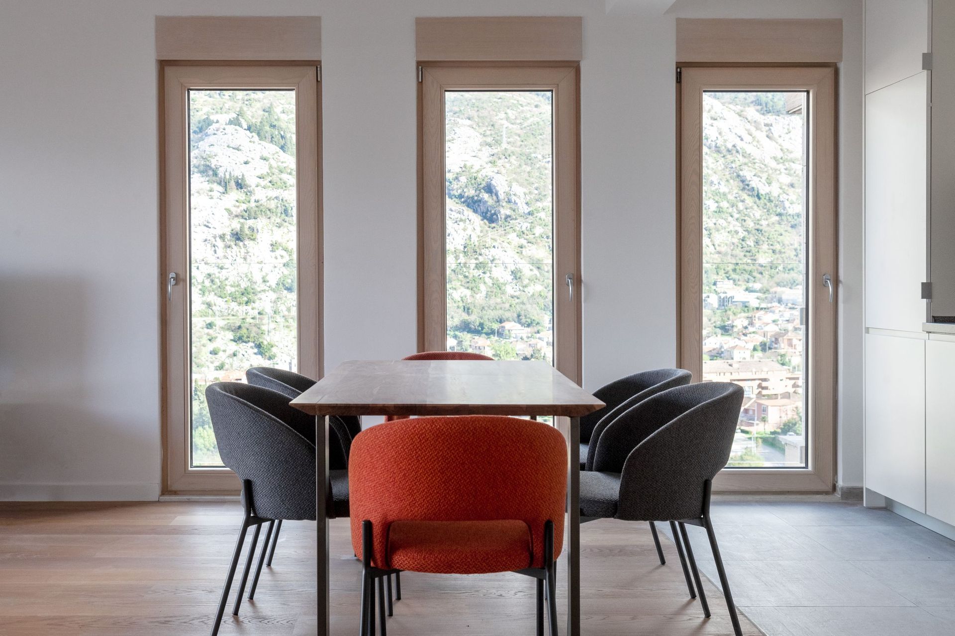 Dining area in a modern apartment in Kotor, Montenegro: wooden table, gray and orange chairs, mountain view.