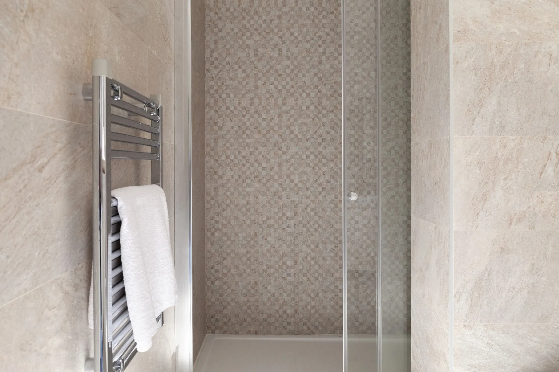 Bathroom featuring a glass shower enclosure and a chrome heated towel rail mounted on beige tiled walls.