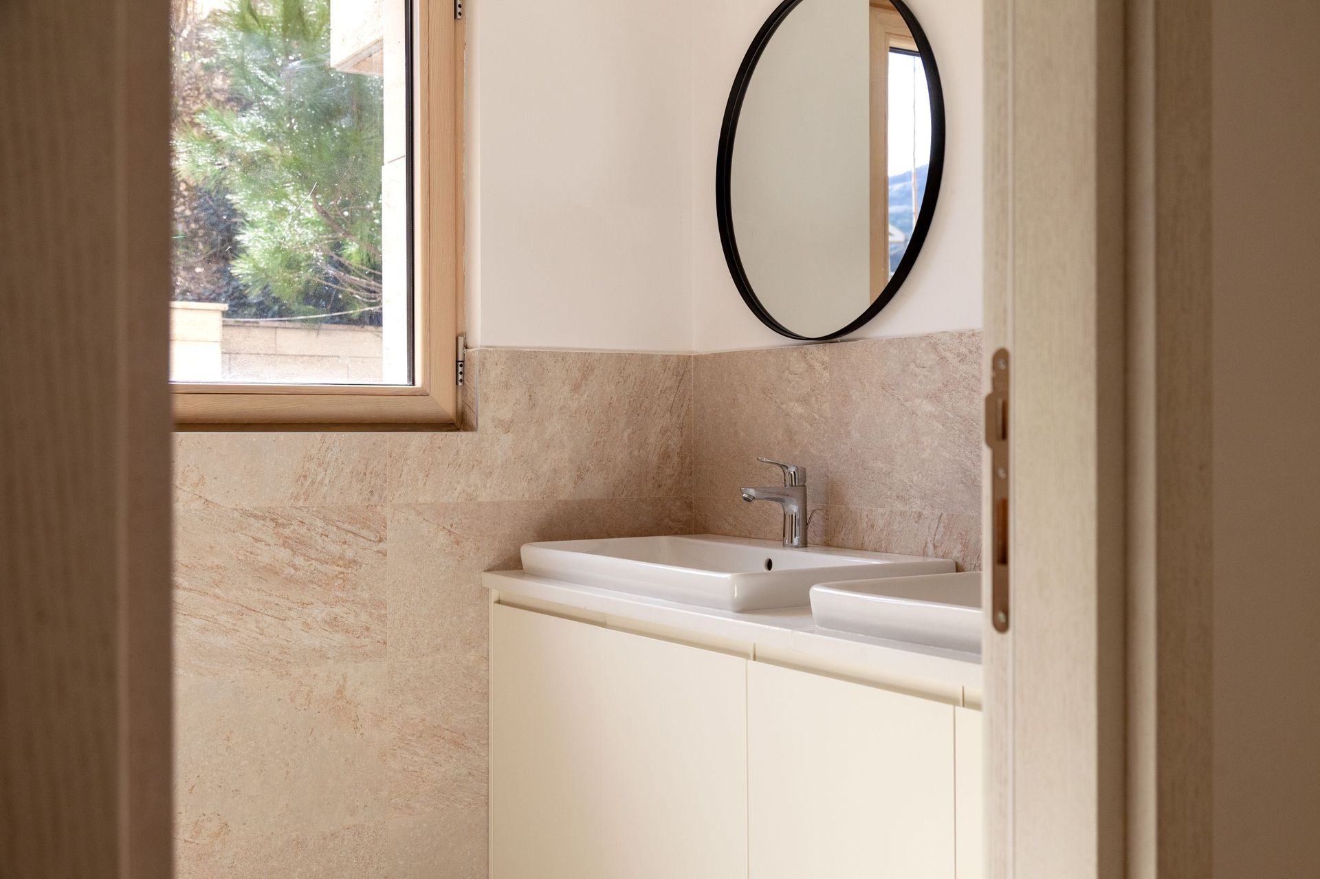 Modern bathroom with a double sink in an apartment in Kotor, Montenegro: beige tiles and a round mirror.