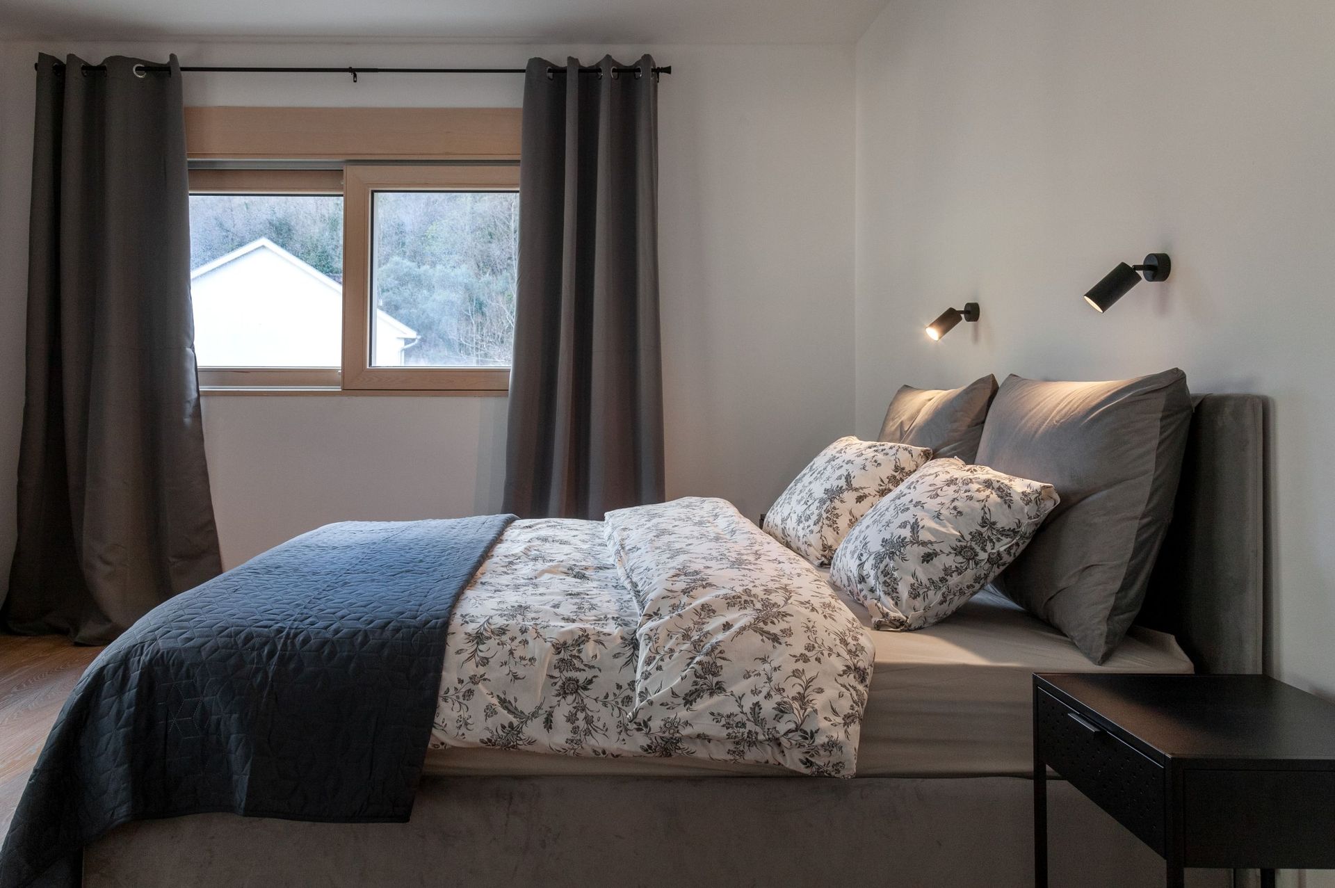 Modern bedroom in an apartment in Kotor, Montenegro: double bed, gray textiles, and a mountain view from the window.