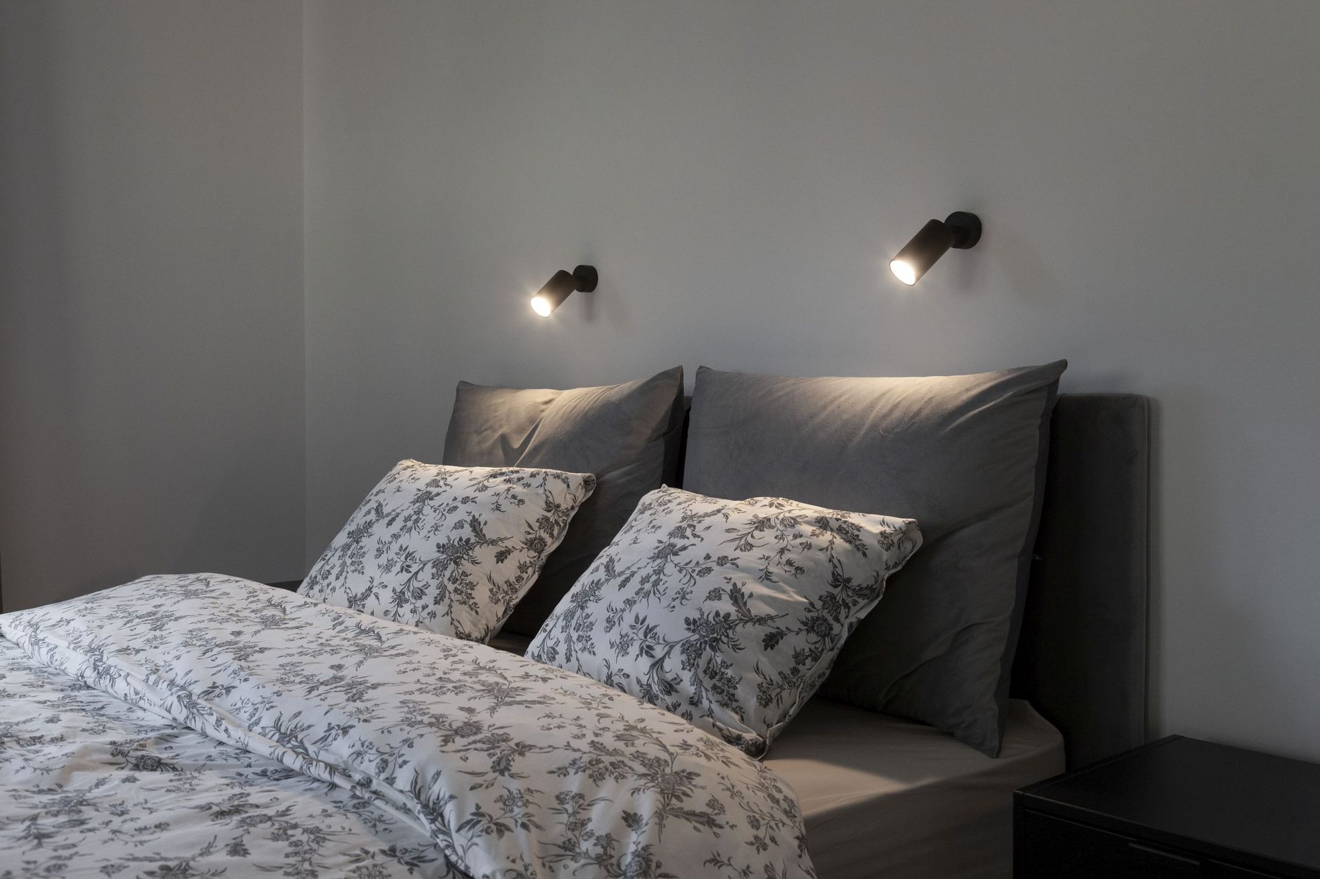 Modern bedroom in an apartment in Kotor, Montenegro: a double bed with gray textiles and wall lights.