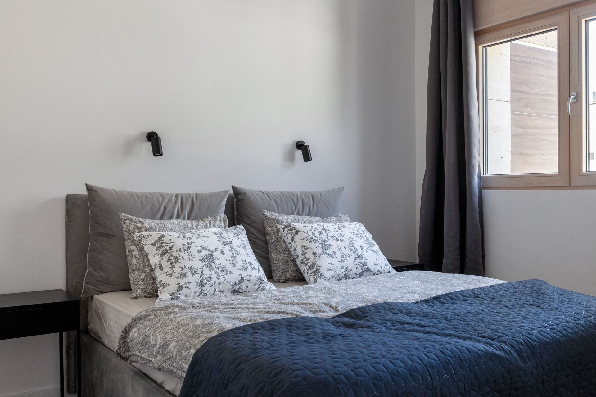 Modern bedroom with a double bed in an apartment in Kotor, Montenegro: gray textiles and stylish wall lamps.