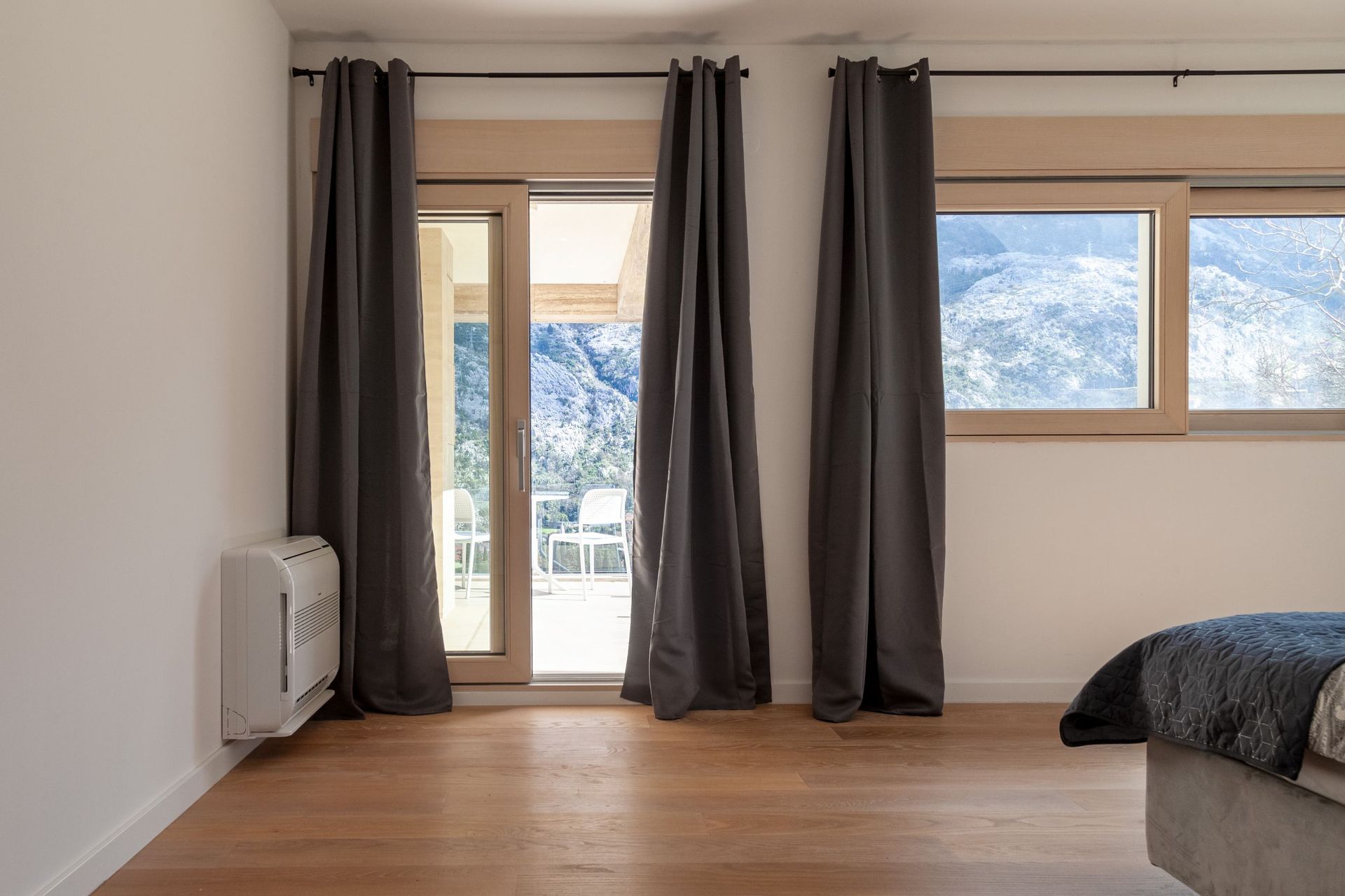 Bedroom in an apartment in Kotor, Montenegro: panoramic windows, access to a terrace with mountain views, parquet flooring, and gray curtains.