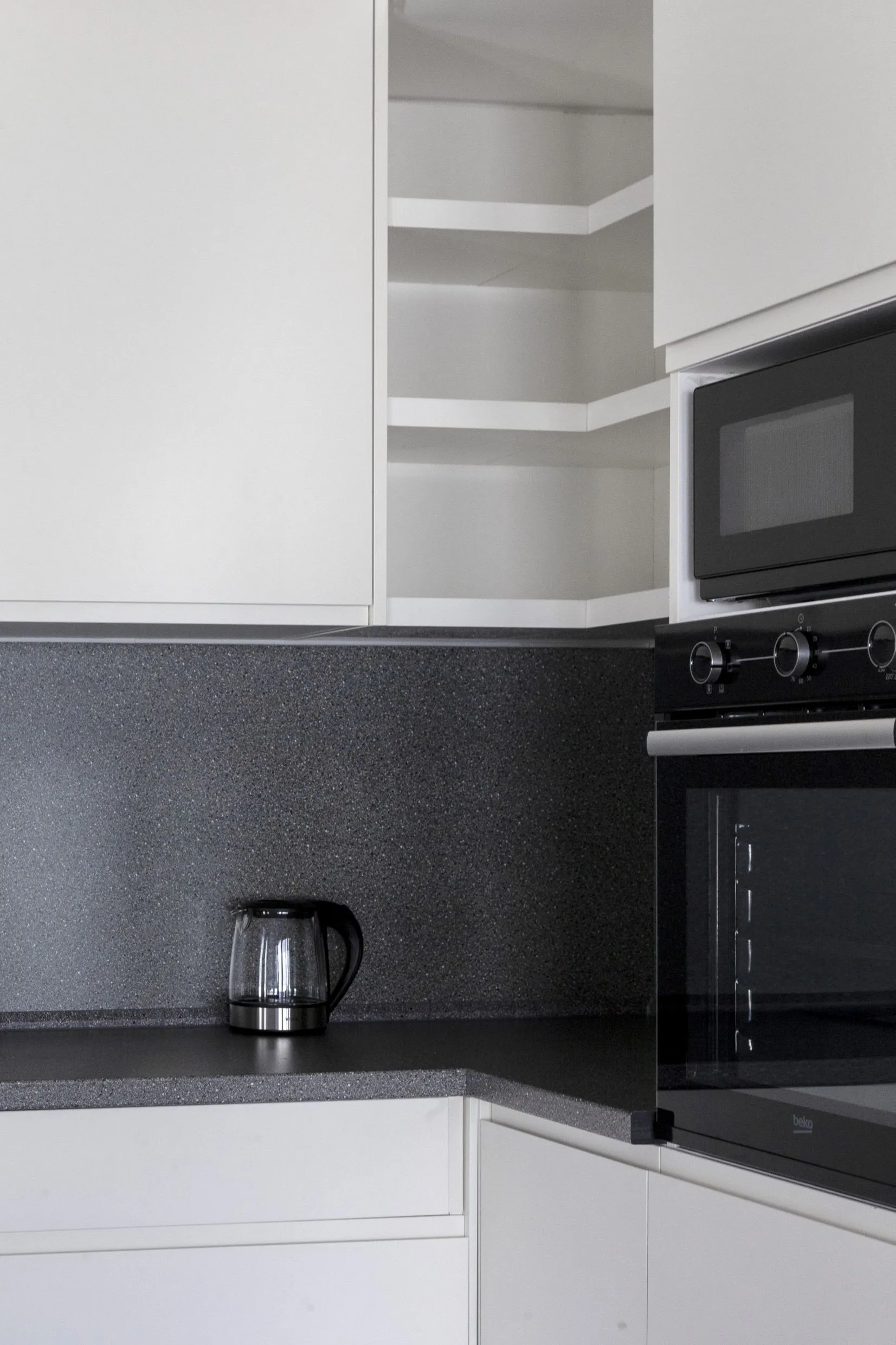 Modern kitchen with white cabinets, dark countertop, built-in oven, microwave, and a glass electric kettle.