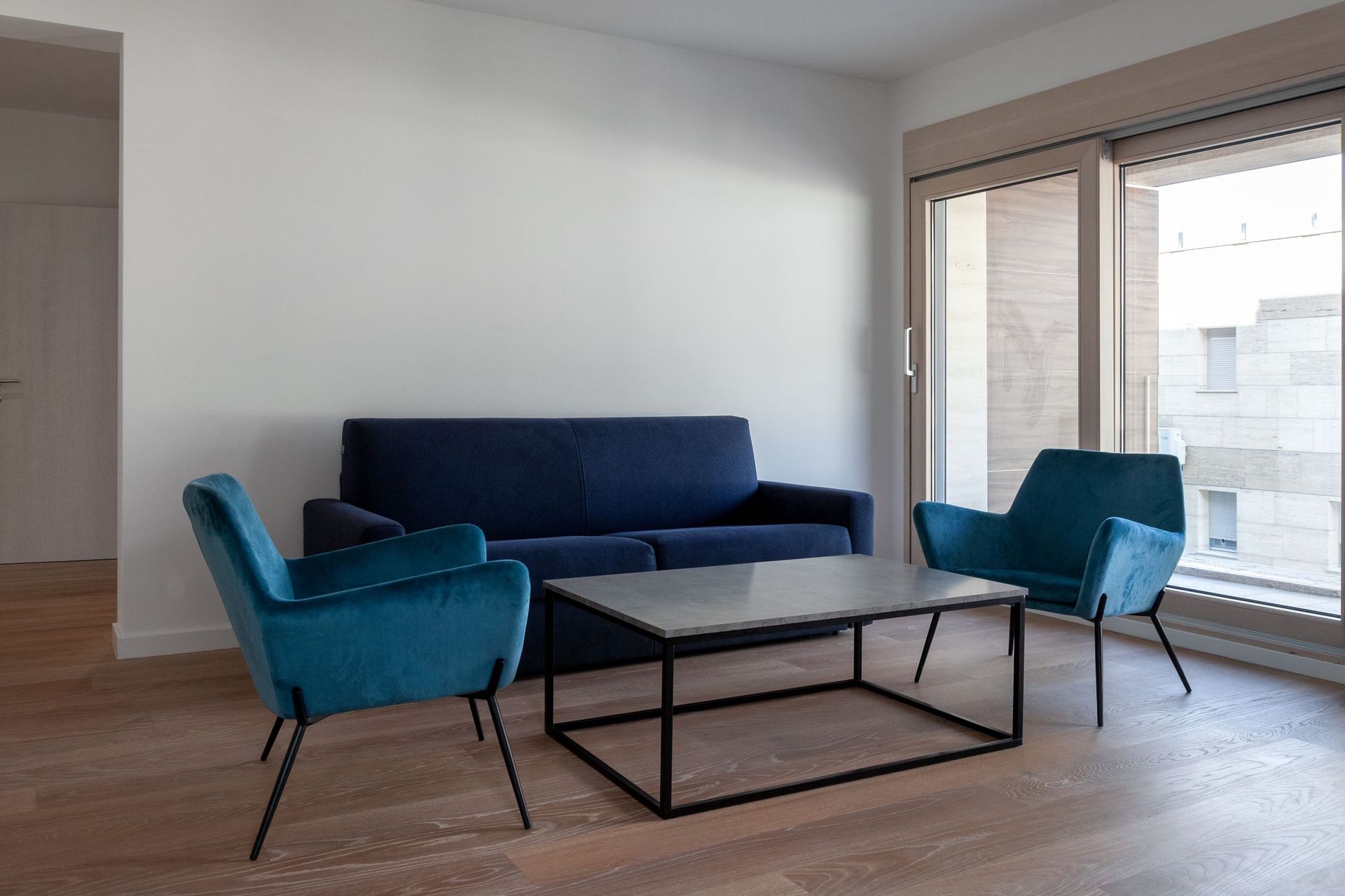 Modern living room with a blue sofa and armchairs in an apartment in Kotor, Montenegro, with a panoramic window and parquet flooring.