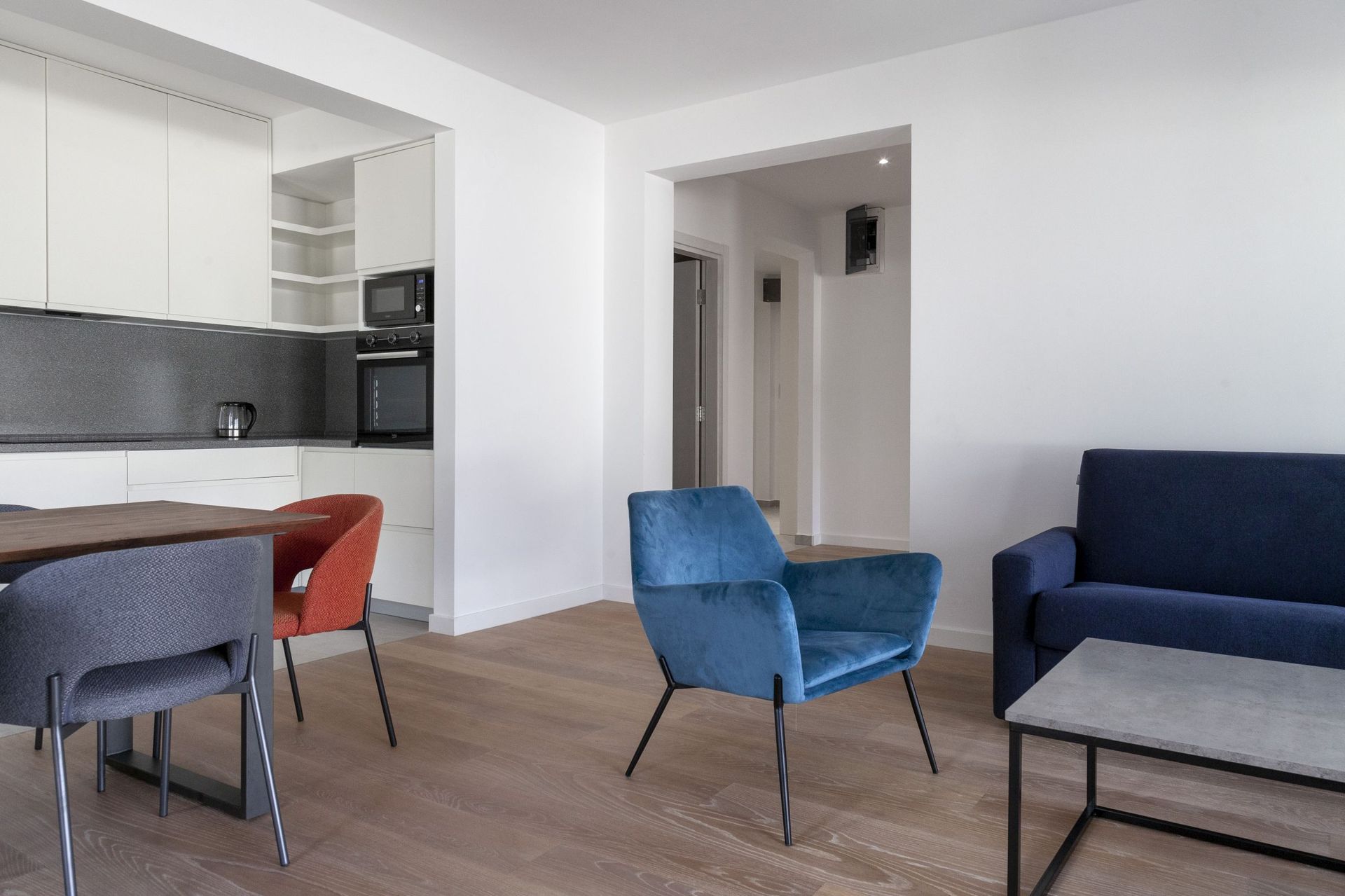 Modern living room with kitchen in an apartment in Kotor, Montenegro: blue armchairs, dining area, and light finishes.