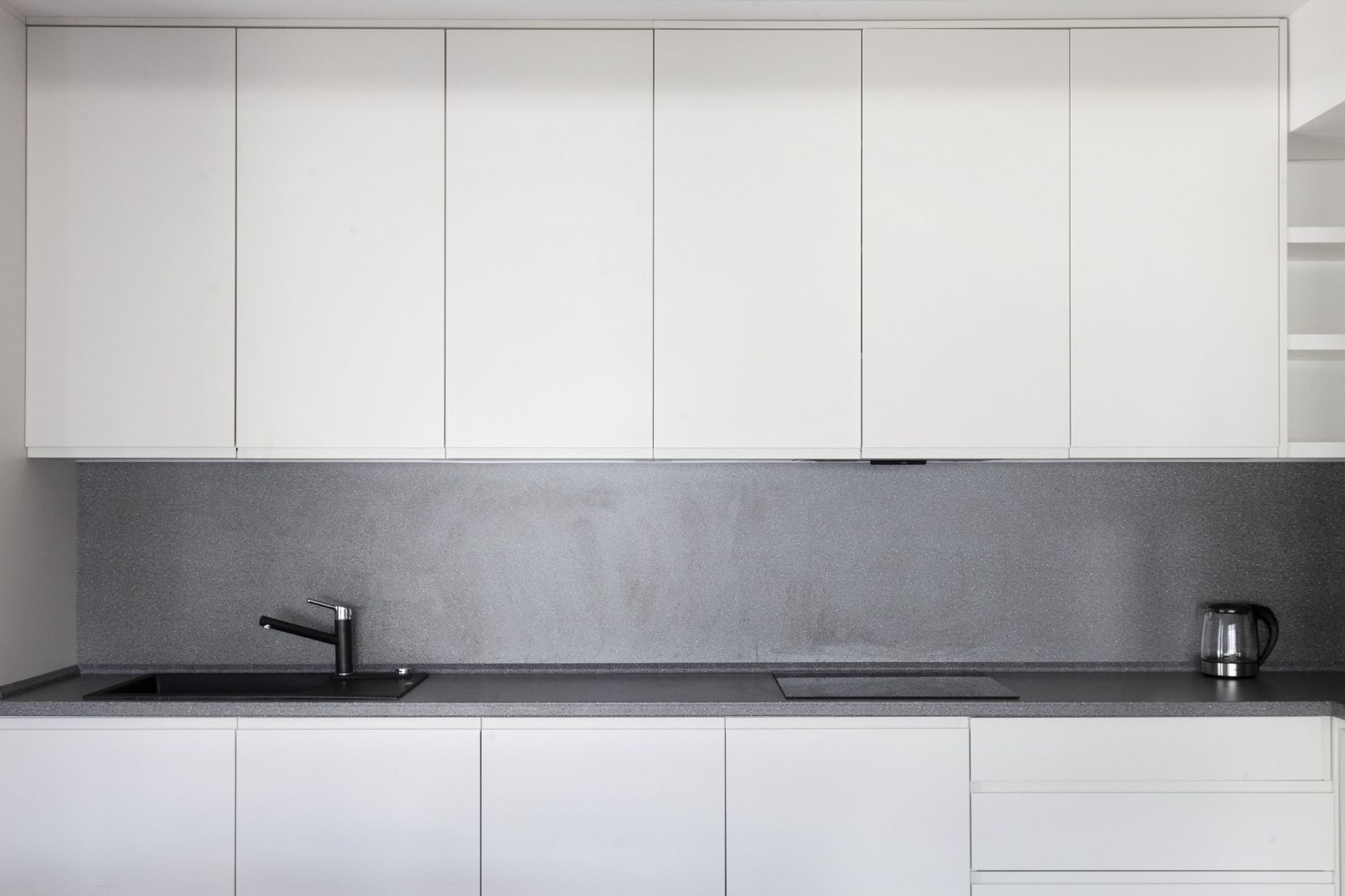 Modern white kitchen with a gray backsplash in an apartment for sale, Kotor, Montenegro. Built-in appliances and sink.