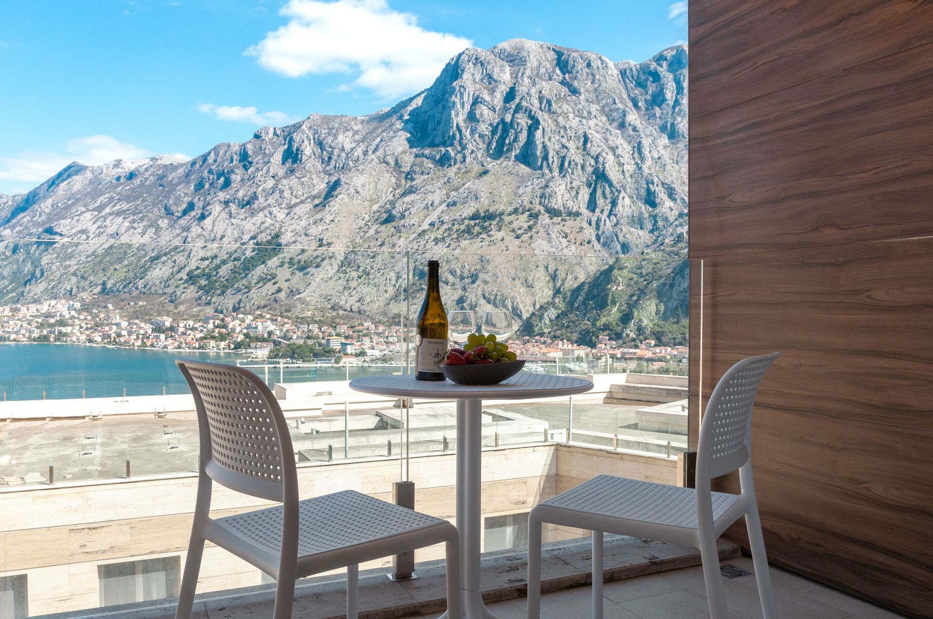 Balcony with a view of the Bay of Kotor and mountains in an apartment, Kotor, Montenegro: table with wine and fruit, modern design.