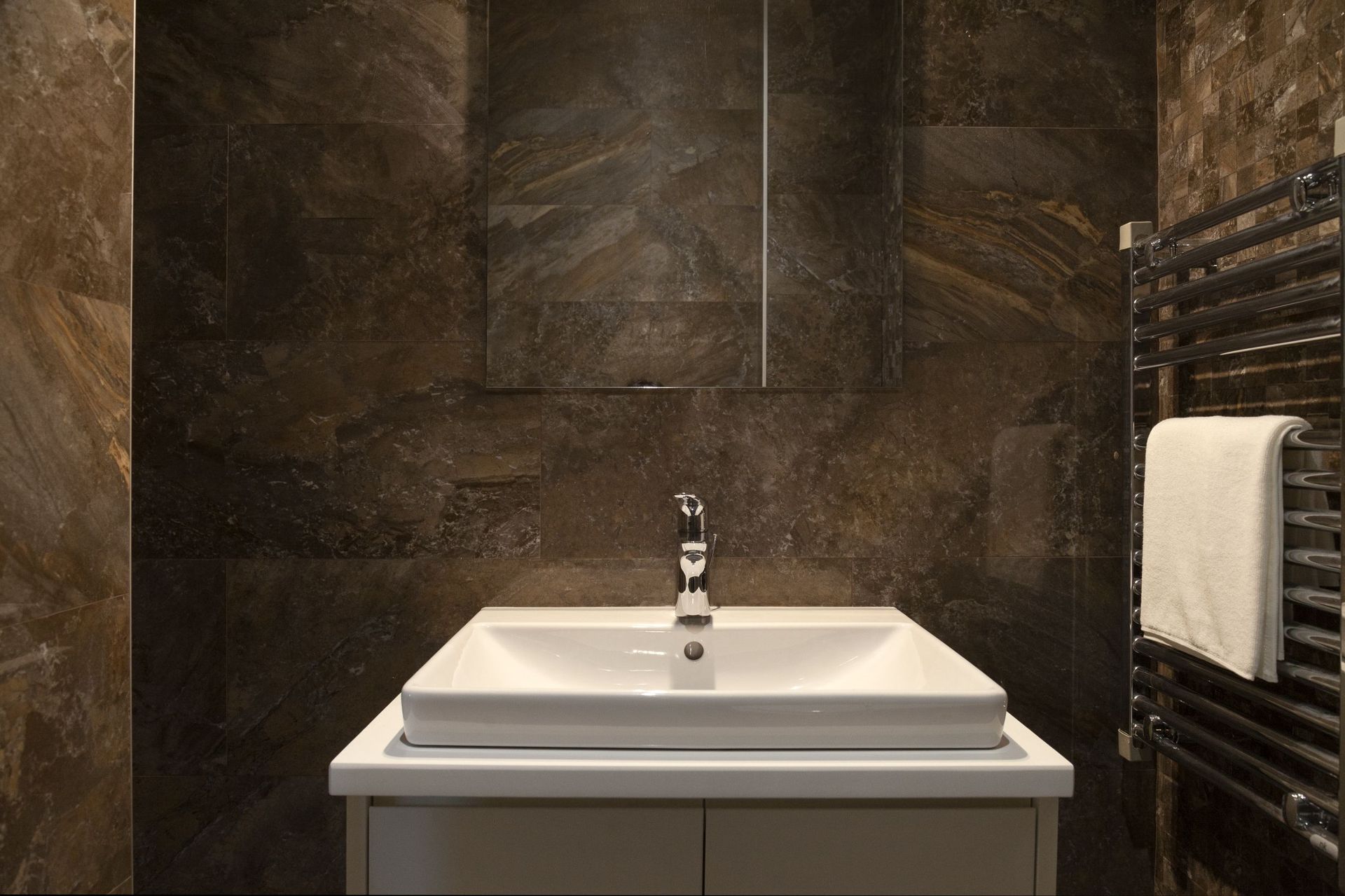 Modern bathroom with dark marble finish in an apartment in Kotor, Montenegro: sink and towel warmer.