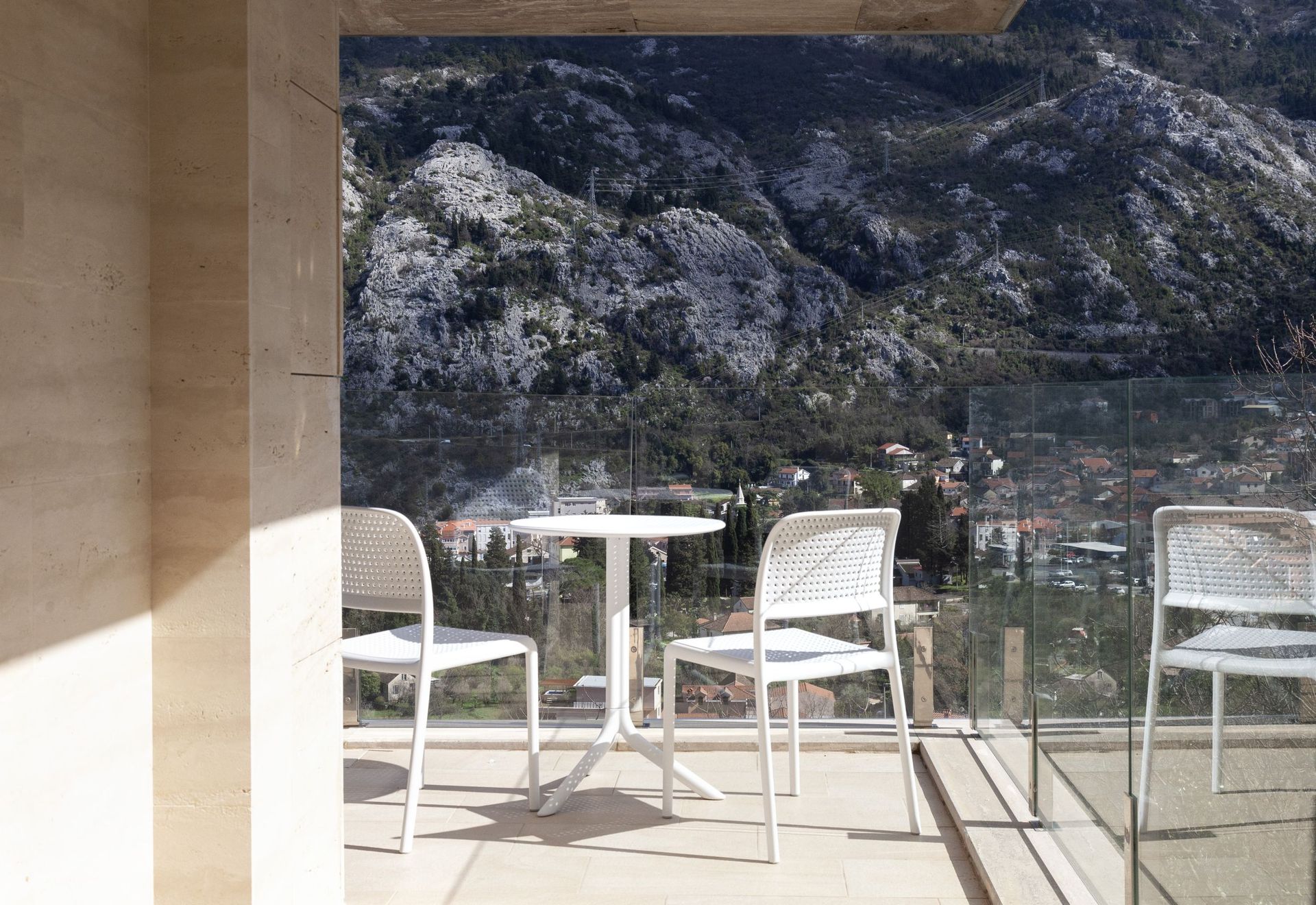 Balcony with white furniture and panoramic views of the mountains and the city of Kotor, Montenegro. Modern finishes and glass railing.
