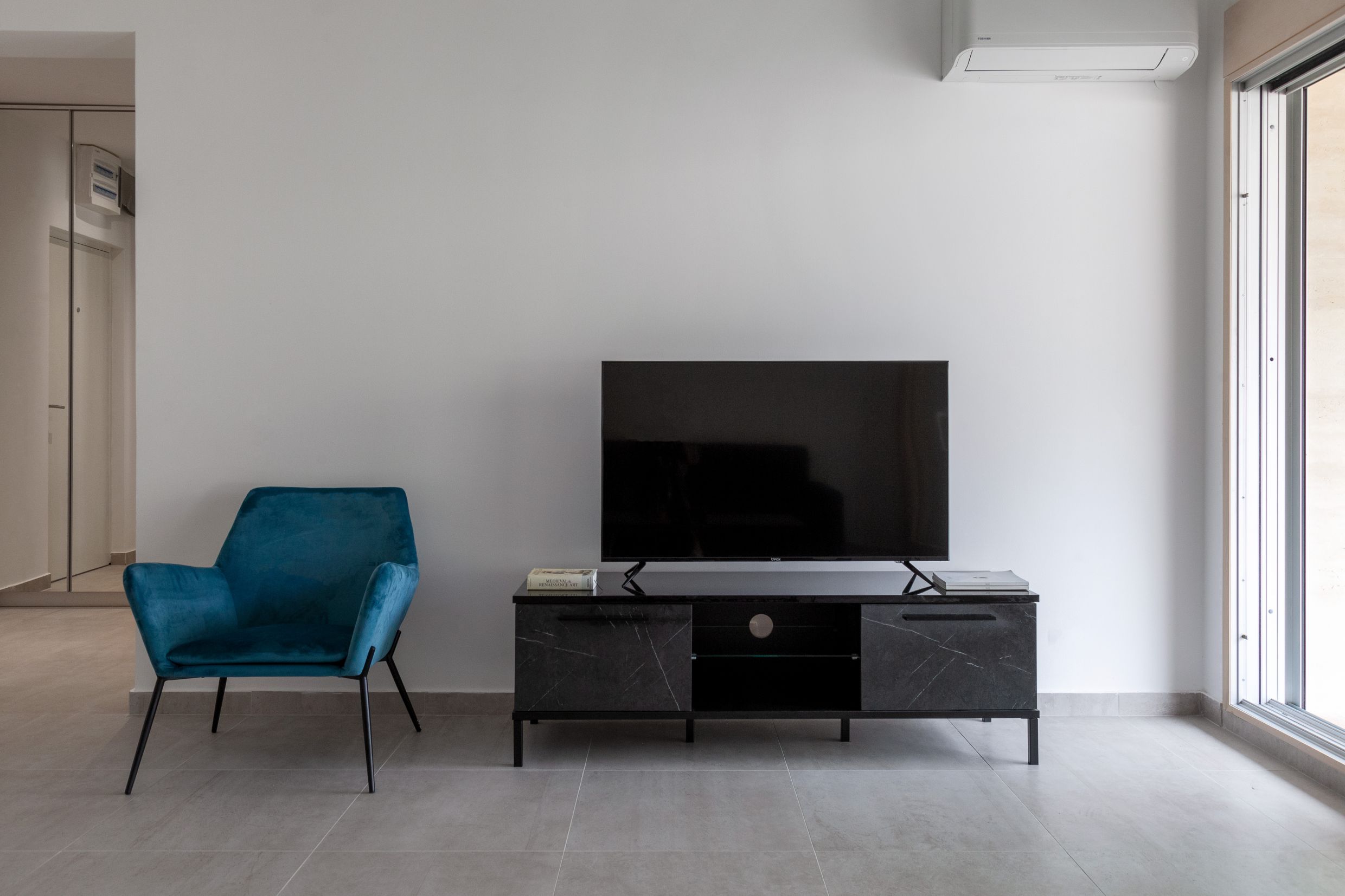 Modern living room in an apartment in Kotor, Montenegro: blue armchair, black TV stand, and panoramic window.
