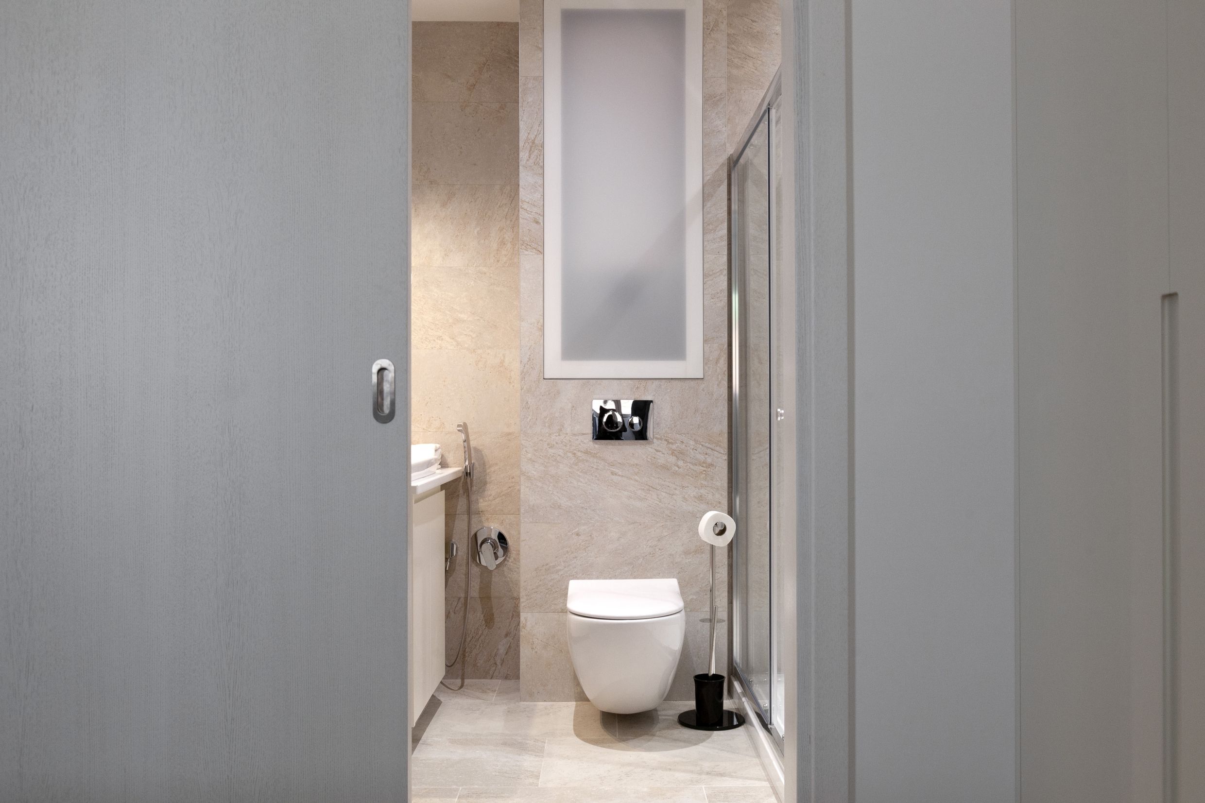 Modern bathroom in an apartment in Kotor, Montenegro: wall-mounted toilet, shower cabin, and beige tiles.