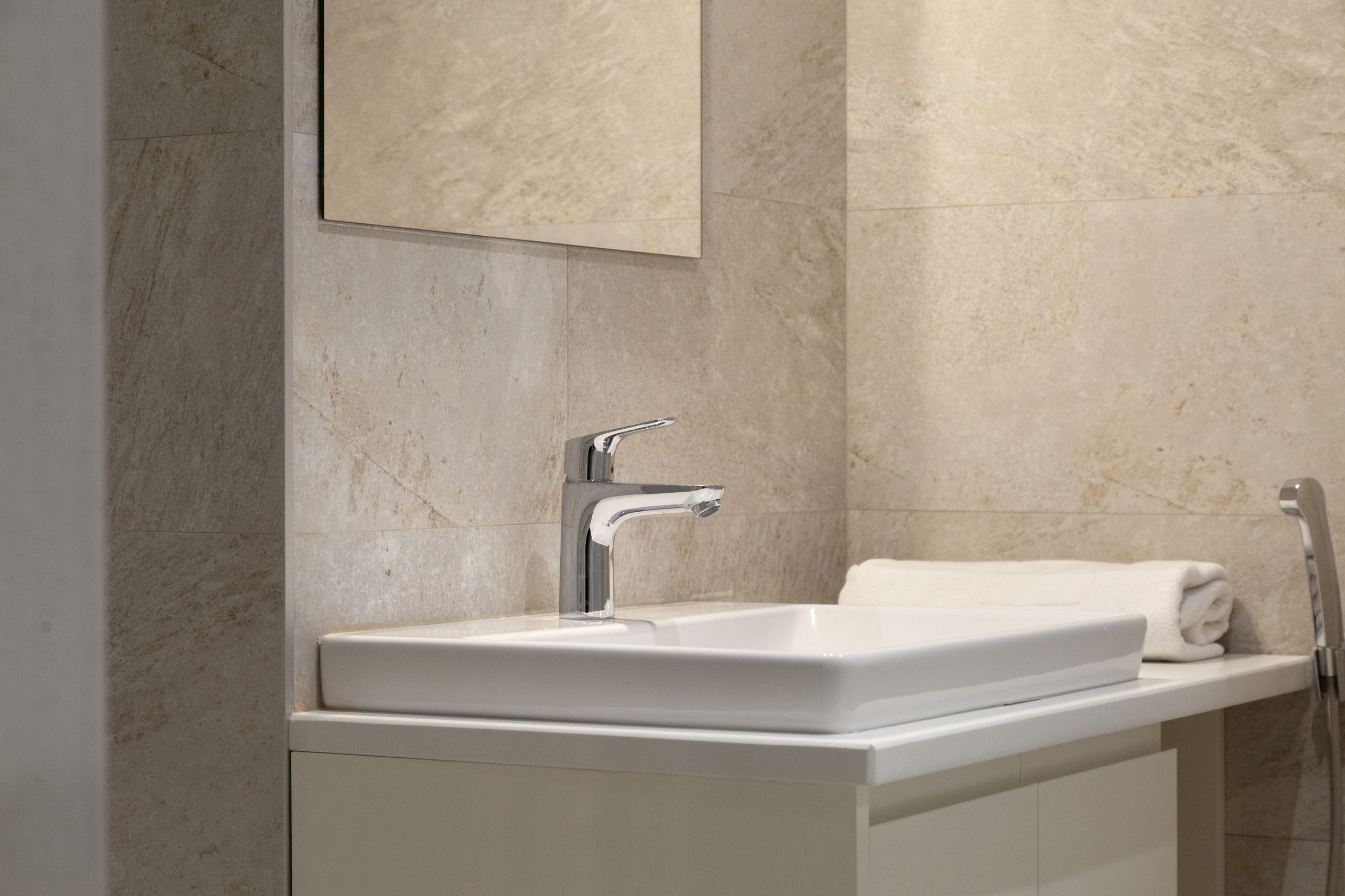 Modern bathroom in an apartment in Kotor, Montenegro: white sink, chrome faucet, and stone-look tiles.
