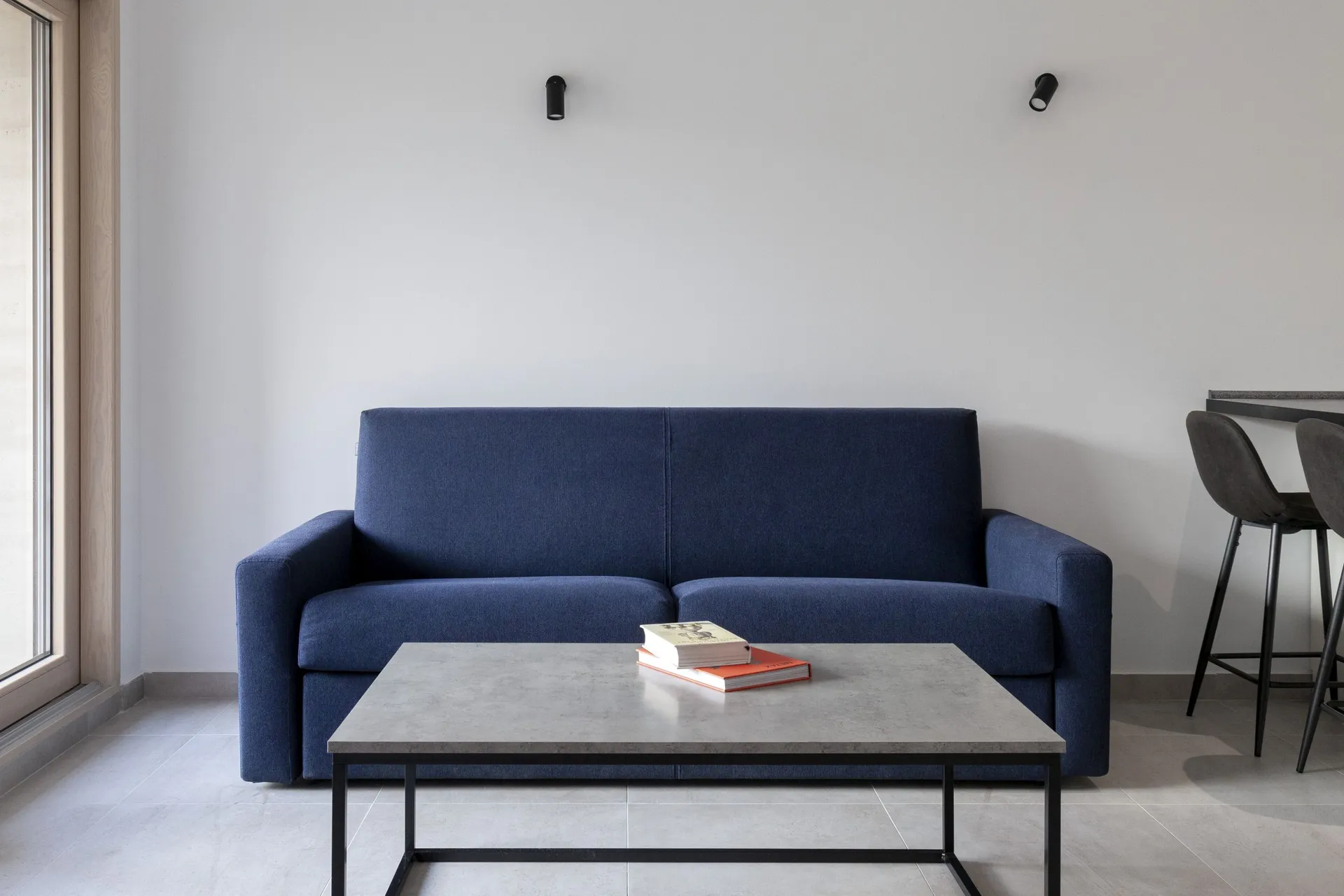 Modern living room with a blue sofa, grey table, and books against a white wall.