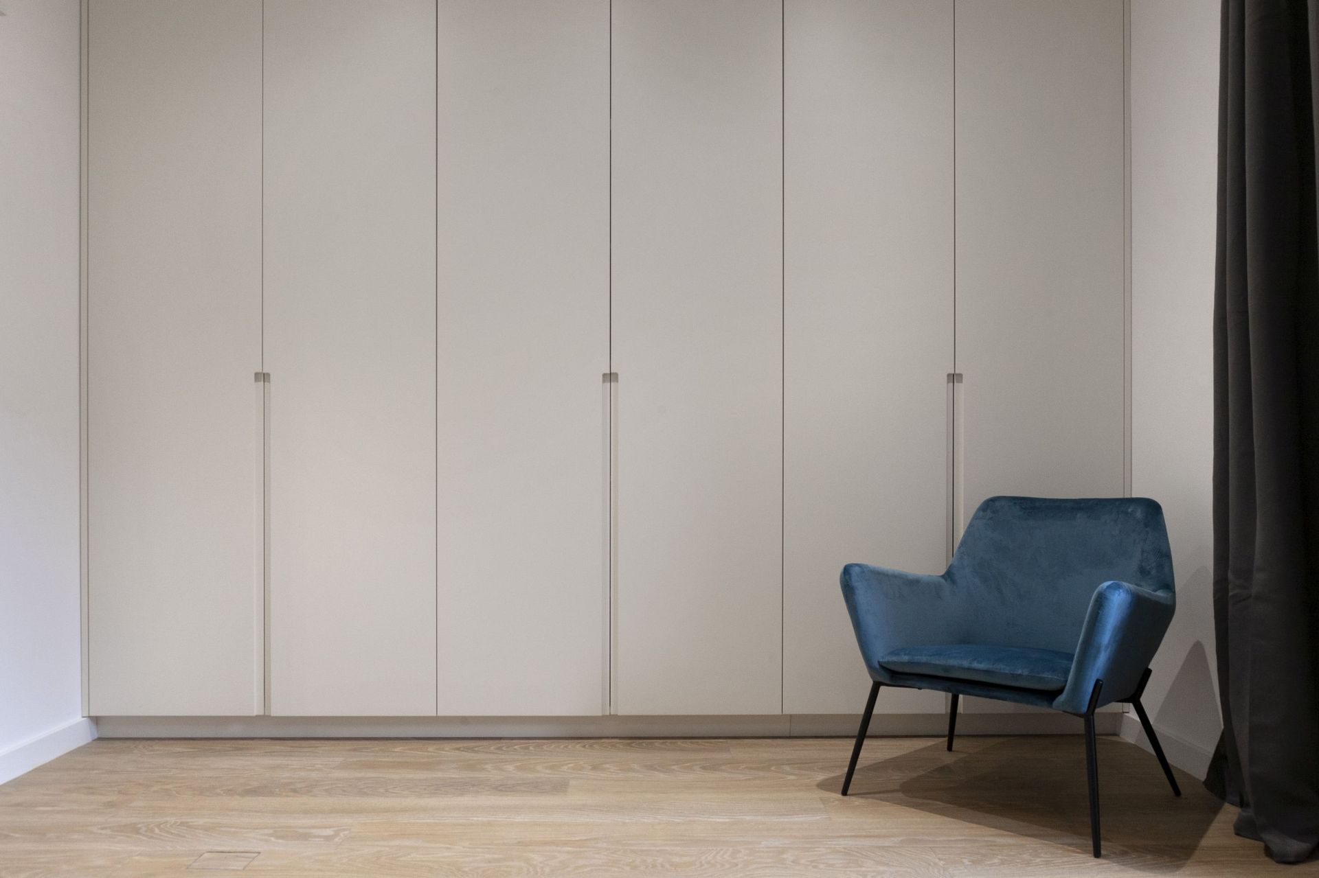 Modern bedroom in an apartment in Kotor, Montenegro: built-in white wardrobe, blue velvet armchair, and parquet floor.