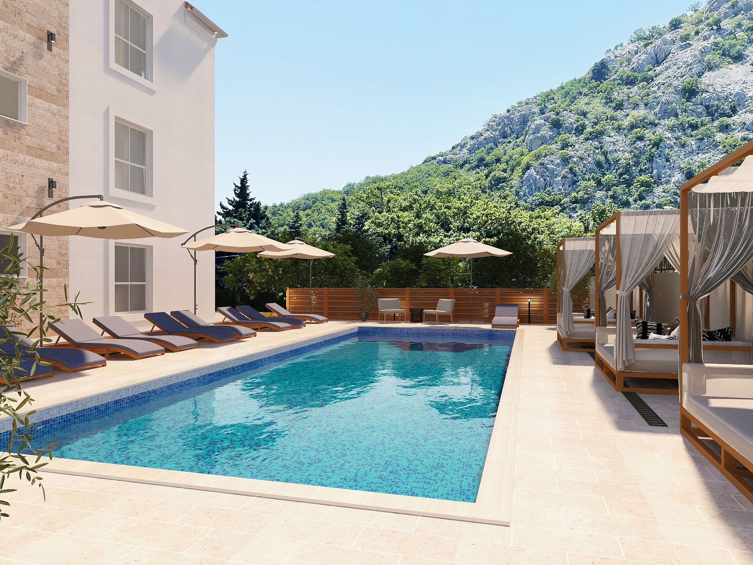 Outdoor swimming pool with sun loungers and cabanas at a residential complex in Sutomore, Montenegro, set against a backdrop of mountains and greenery.