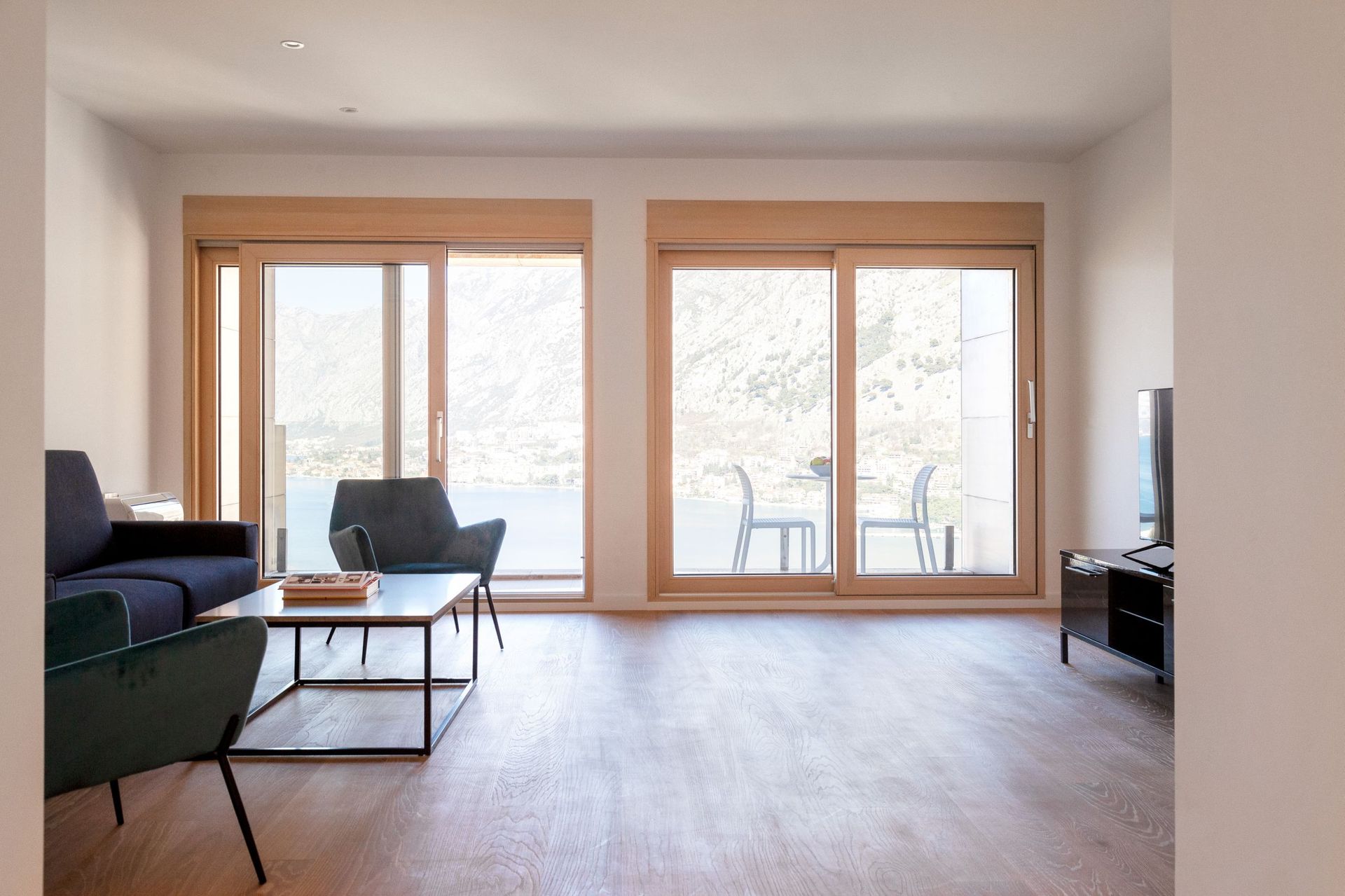 Modern living room in an apartment in Kotor, Montenegro, with panoramic sea and mountain views through sliding windows.