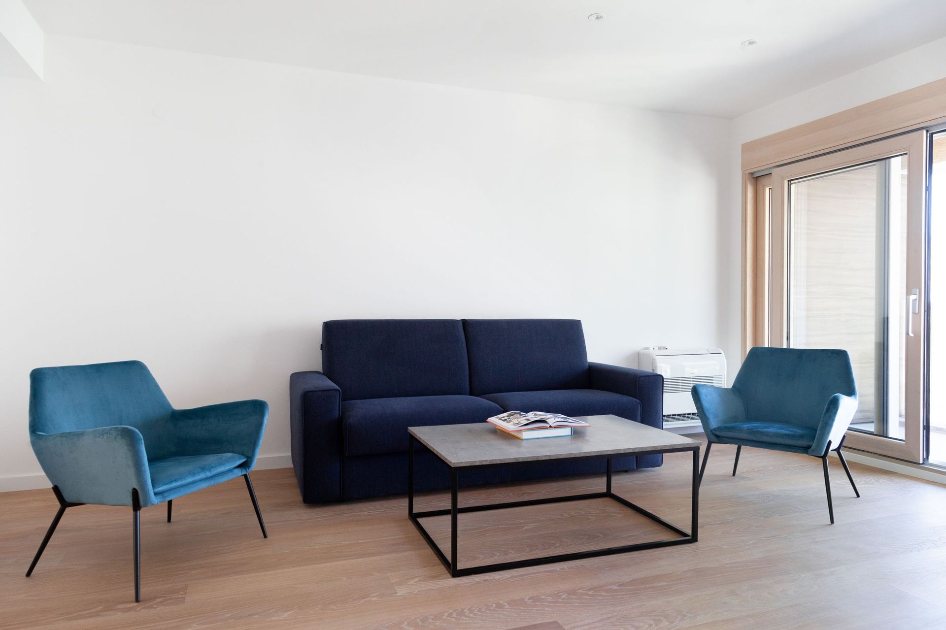 Living room in an apartment in Kotor, Montenegro: blue sofa, two armchairs, coffee table, and a panoramic window with access to the balcony.
