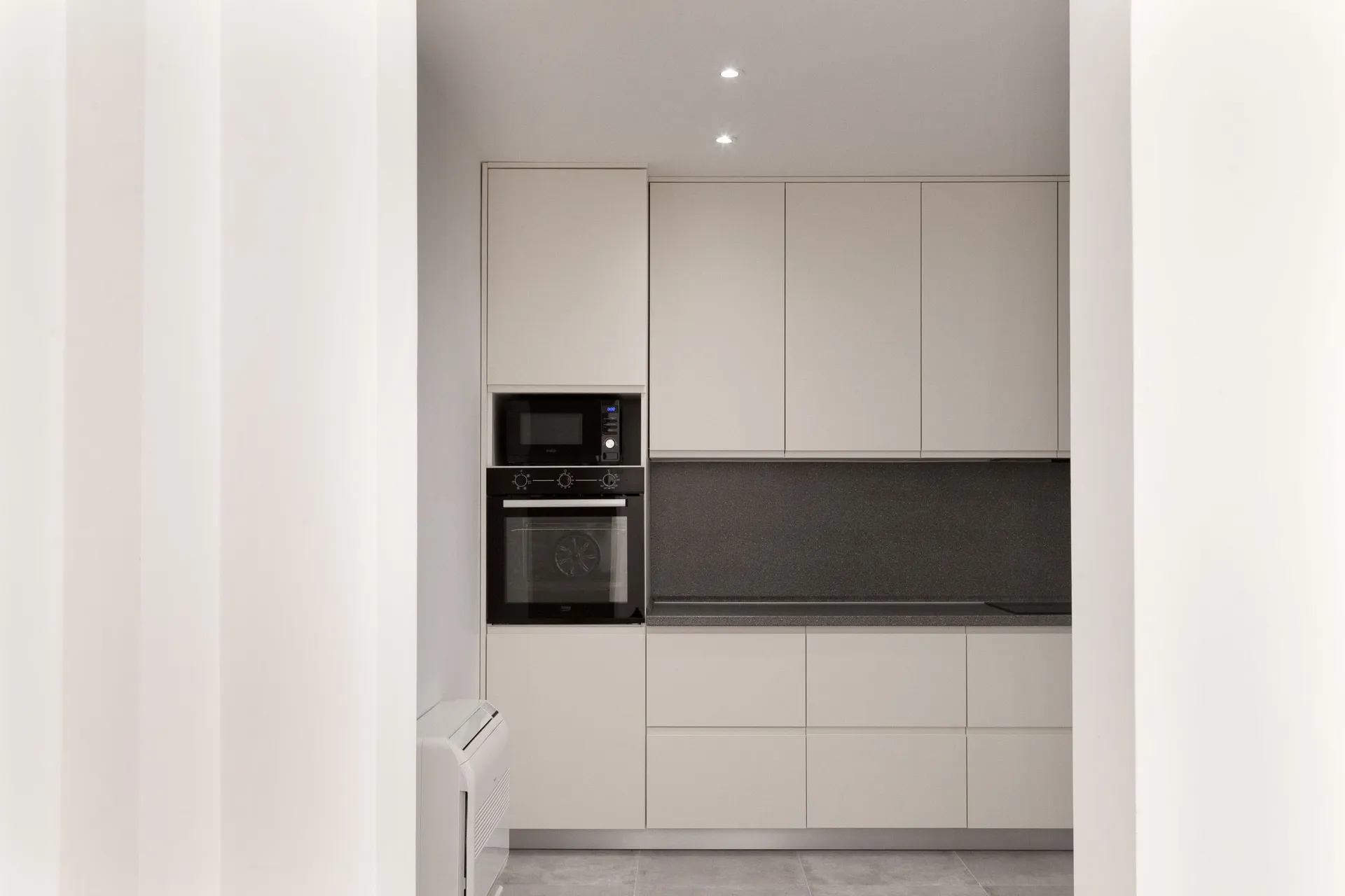 Modern kitchen with beige cabinets, black built-in appliances, and dark countertop.