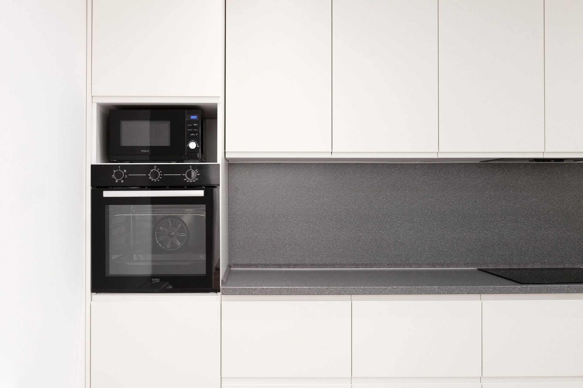 Modern white kitchen with a gray countertop and built-in Beko appliances in an apartment in Kotor, Montenegro.