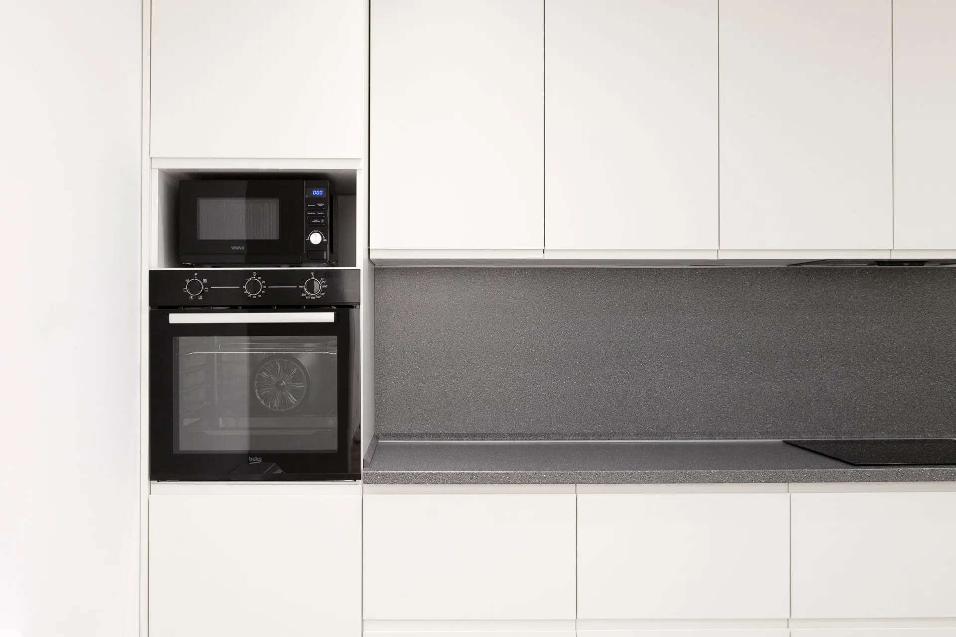 Modern kitchen with white cabinets, black microwave and oven on a grey countertop.