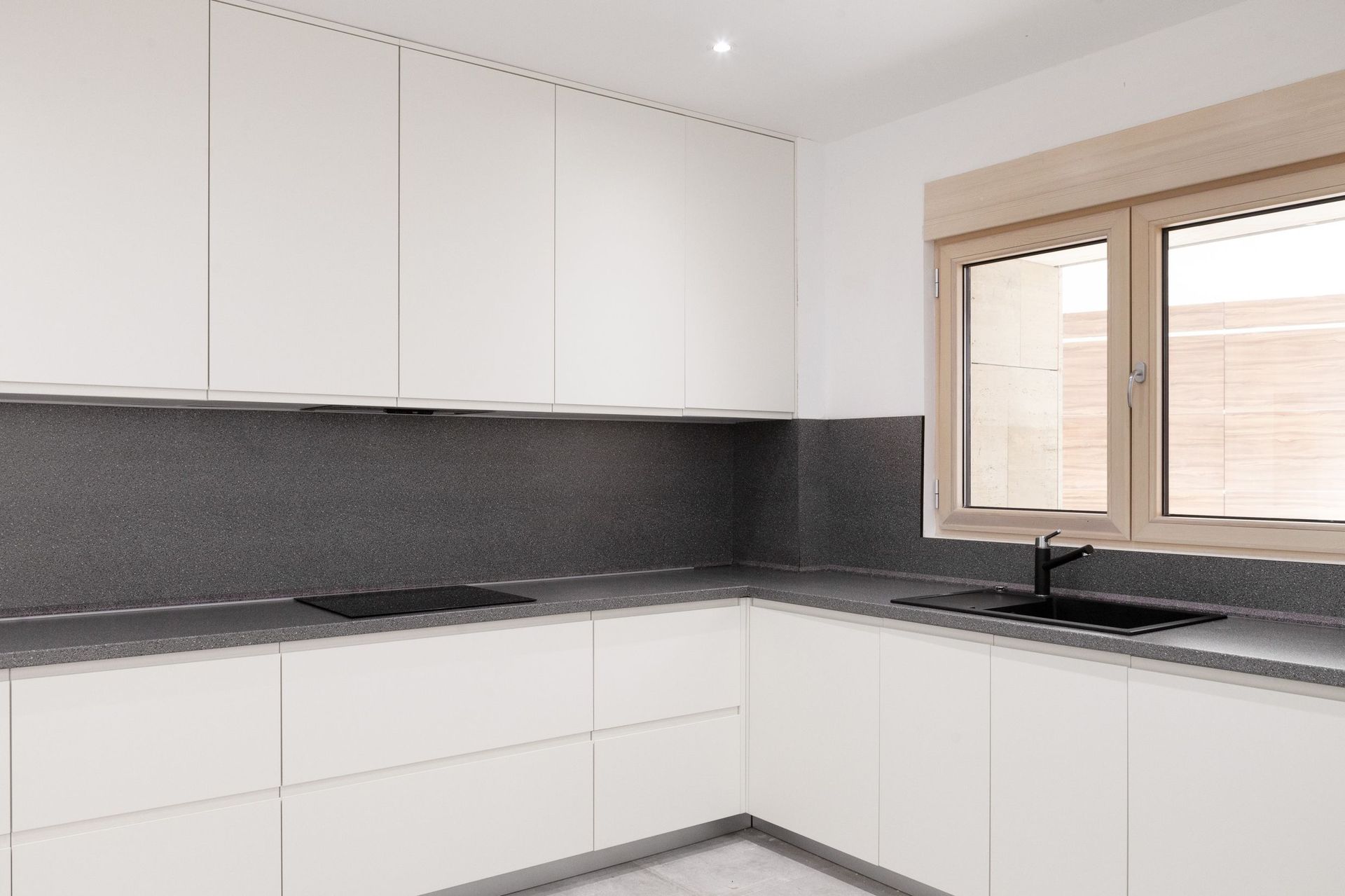 Modern white kitchen with a dark countertop in an apartment, Kotor, Montenegro: built-in appliances and a bright window.