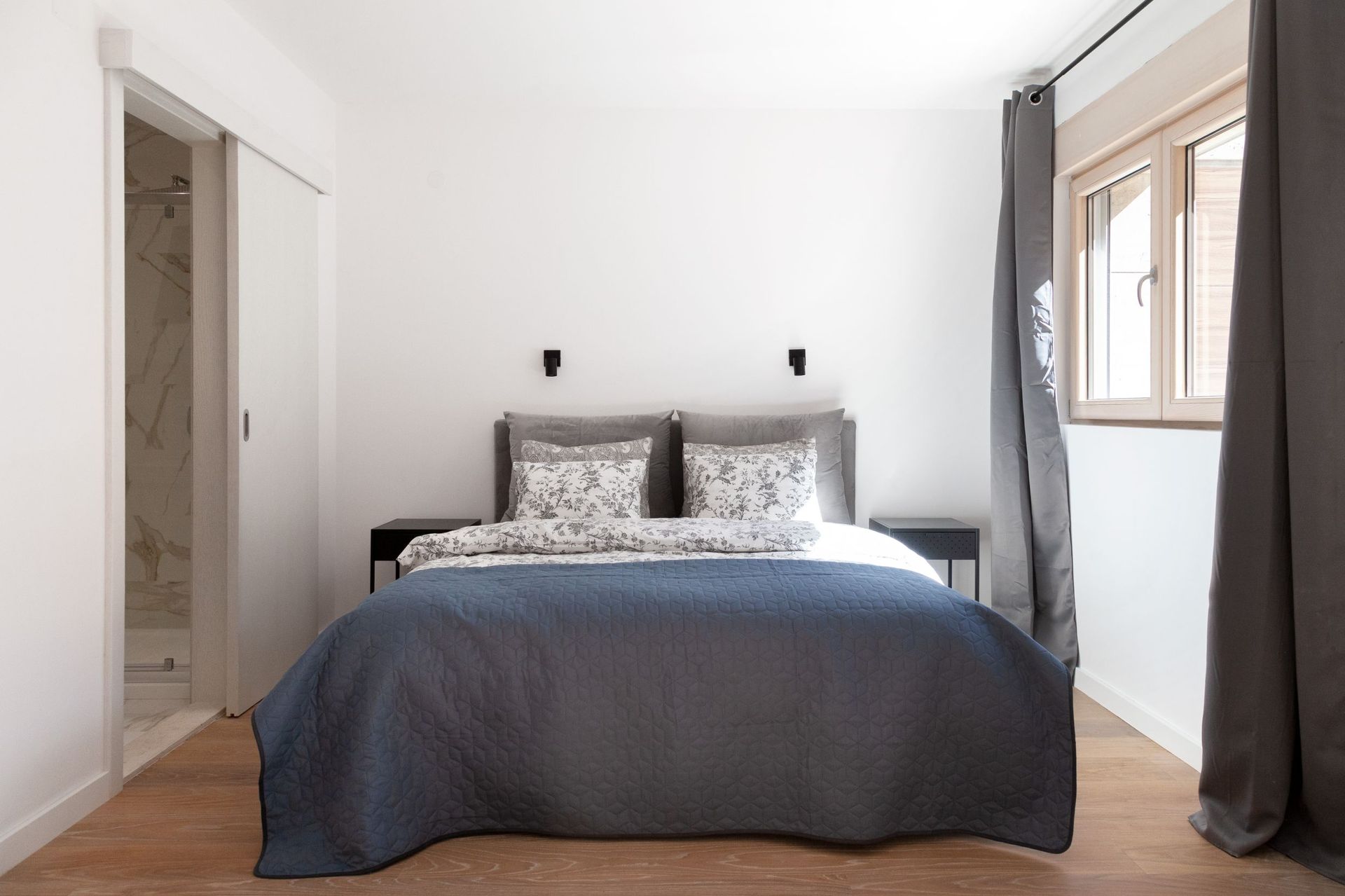 Modern bedroom in an apartment in Kotor, Montenegro: double bed, wooden floor, and entrance to the bathroom.