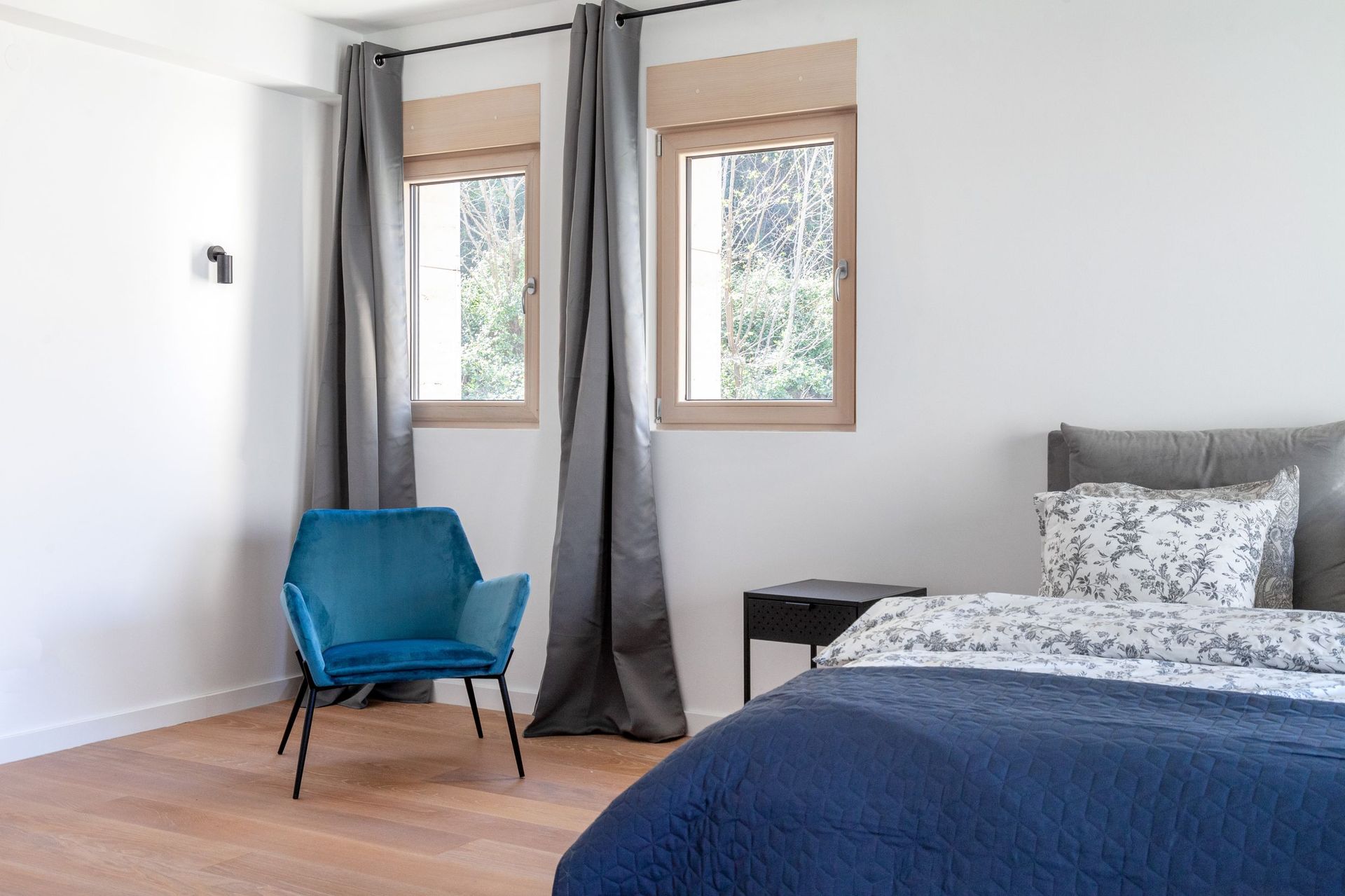 Modern bedroom in an apartment in Kotor, Montenegro: blue armchair, double bed, light parquet flooring, and a view of the garden.