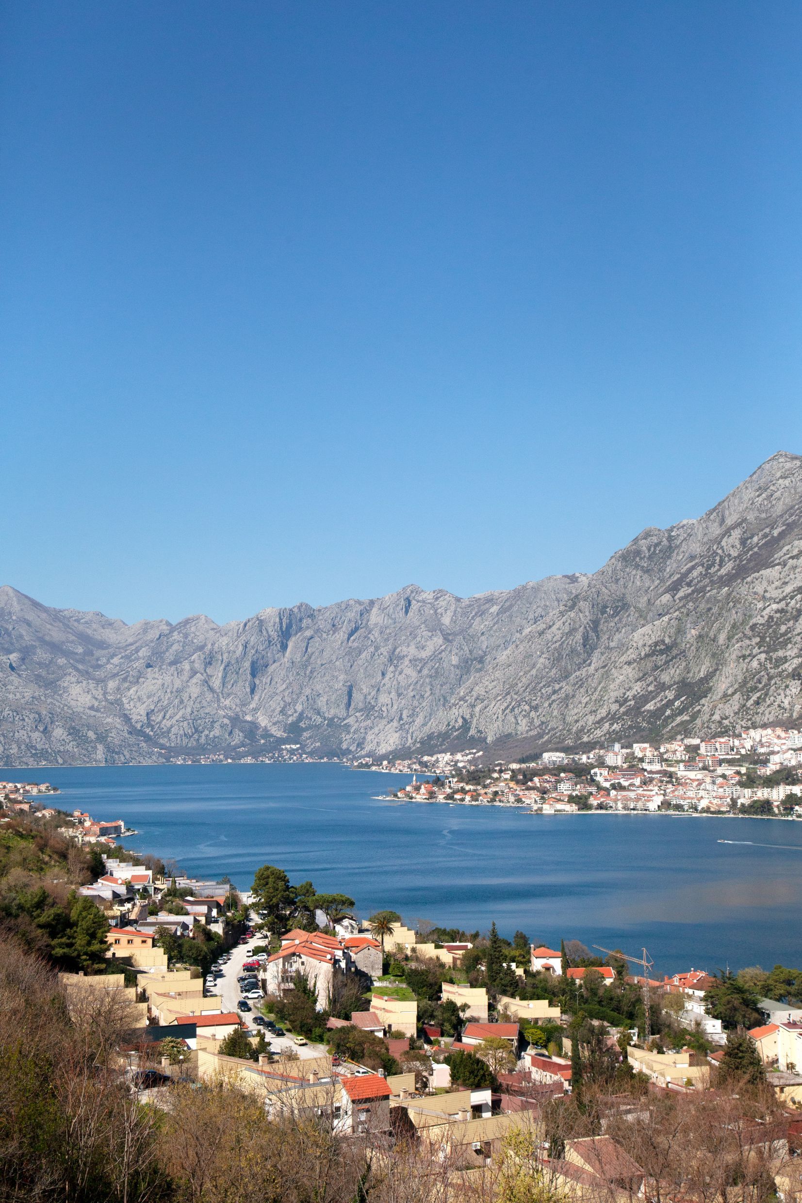 Panoramic view of the Bay of Kotor and mountains in Kotor, Montenegro: coastal houses with red roofs and a sea view.