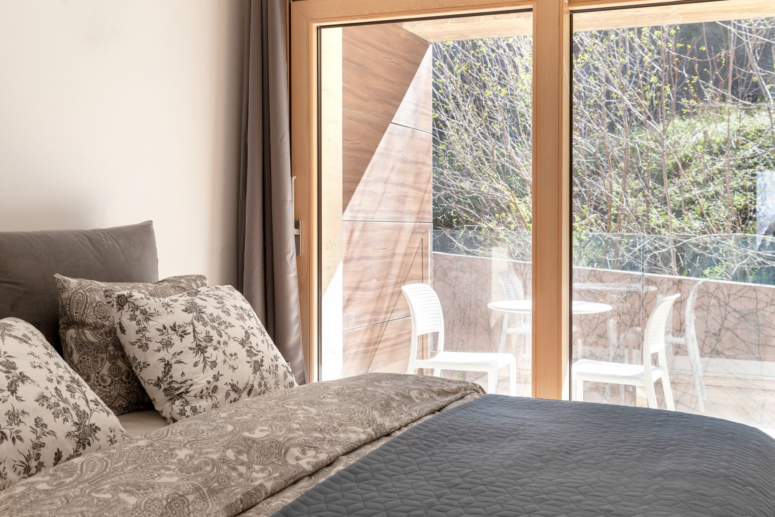 Bedroom in an apartment in Kotor, Montenegro: a double bed, panoramic window, and access to a terrace with garden furniture.