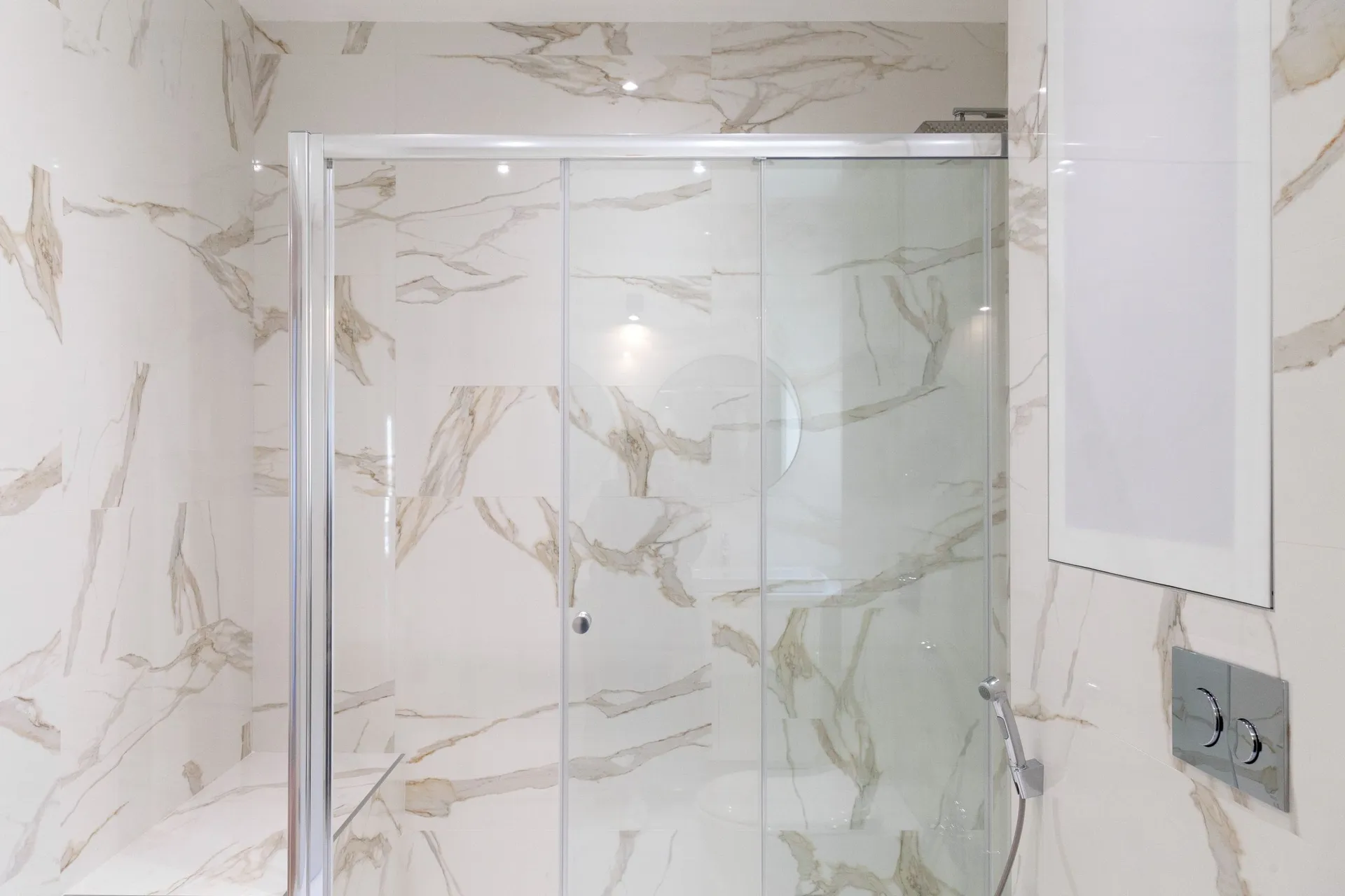 Modern bathroom featuring a glass shower enclosure and white marble-effect wall tiles.