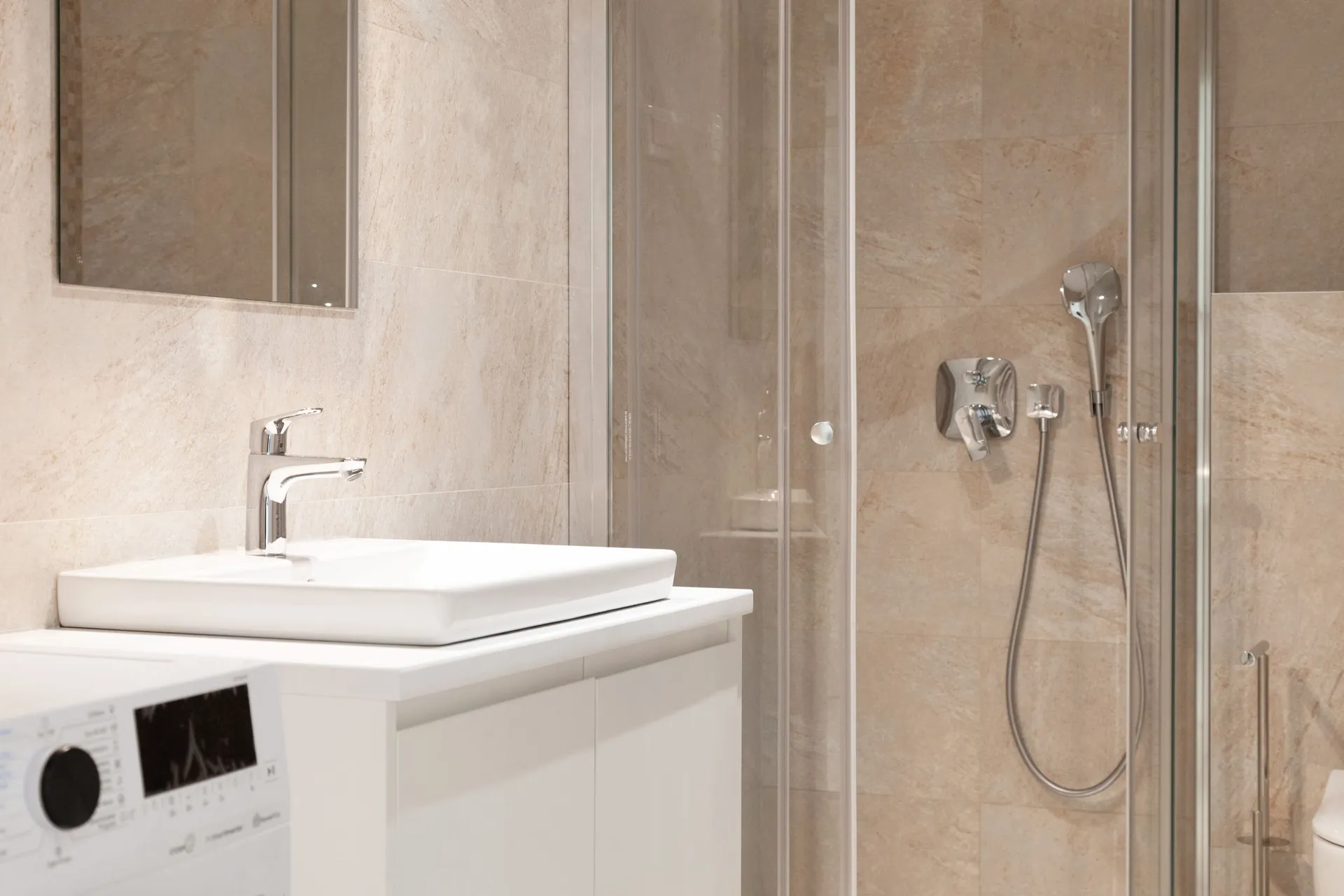 Modern bathroom featuring a white rectangular vessel sink, a glass-enclosed shower with chrome fixtures, and beige stone tiles on the walls.